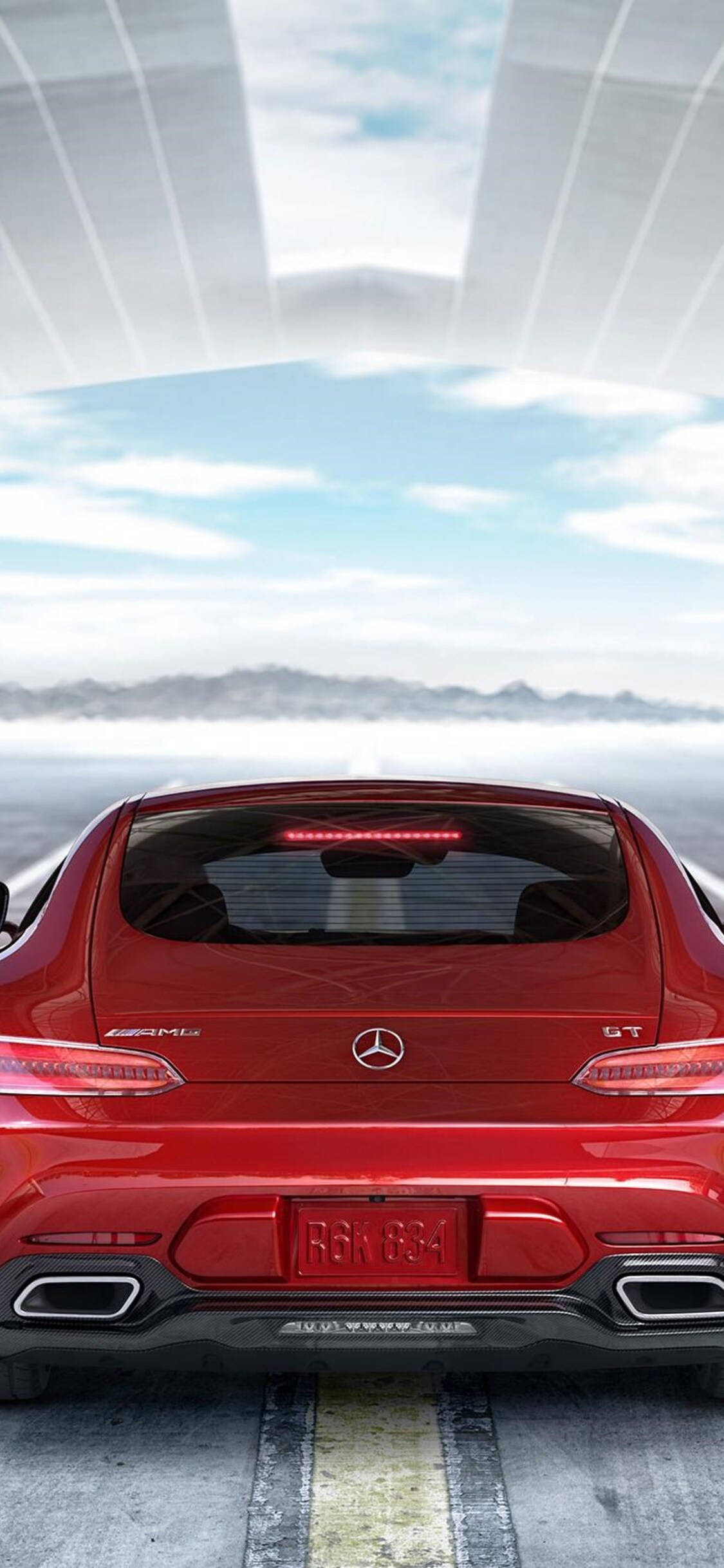 amg iPhone 桌布 壁紙 — 一輛亮紅色的 Mercedes-AMG GT 跑車從後方觀看，行駛在未來風格的玻璃天篷下的道路上，遠方有山脈和天空。