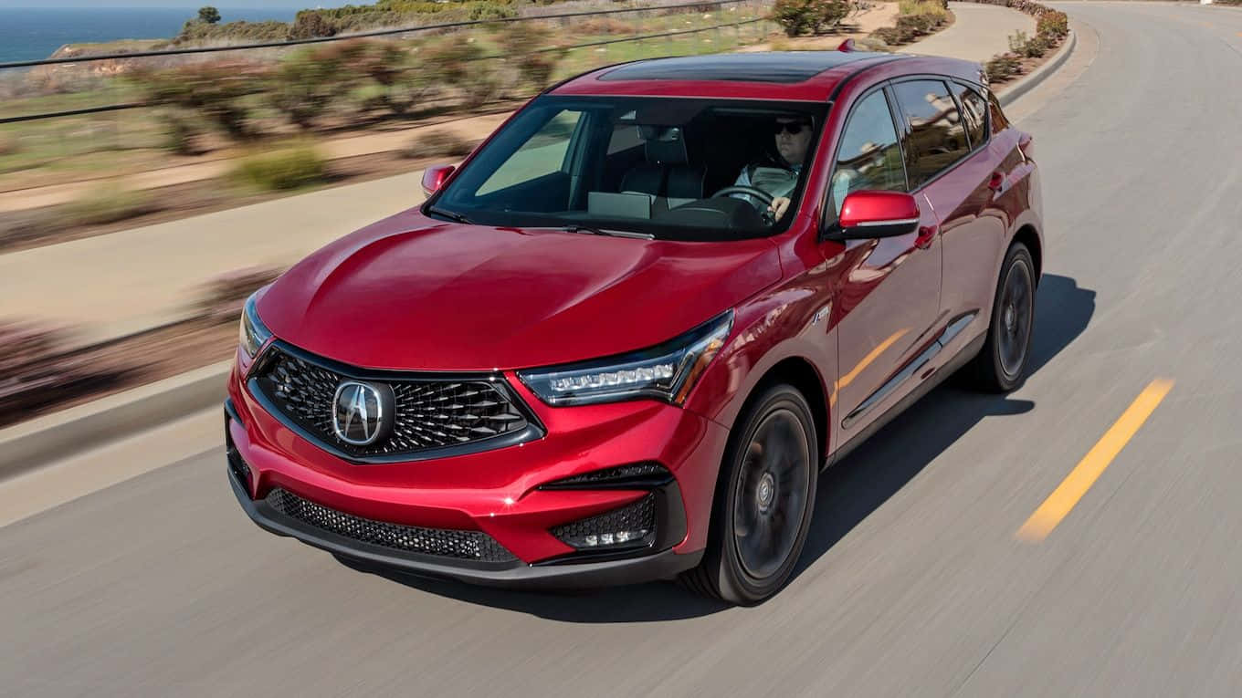 Acura Rdx 桌布 壁紙 — 一輛亮紅色的Acura SUV沿著海岸高速公路疾馳，背景是模糊的綠樹和海洋。