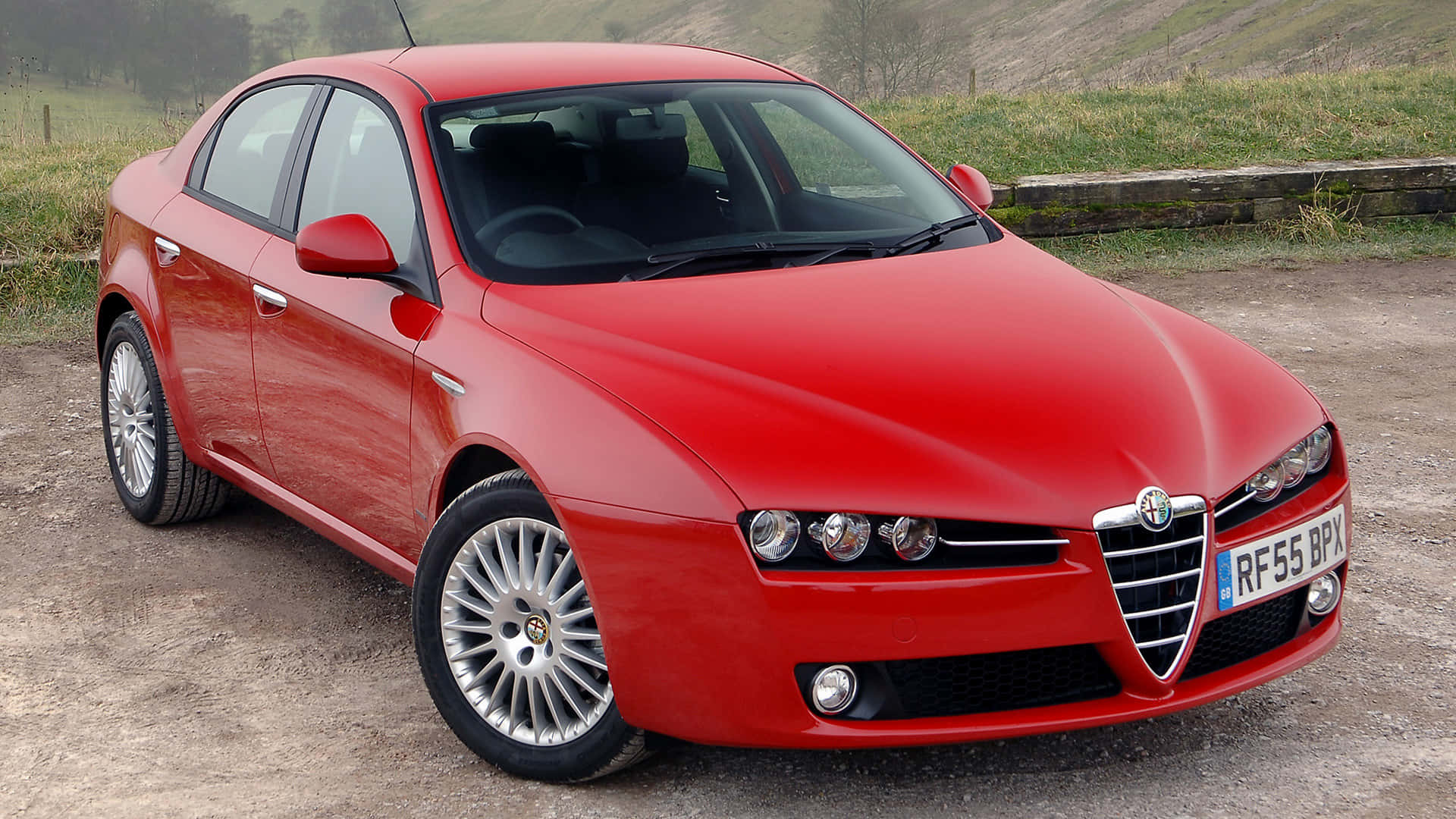 Alfa Romeo 159 桌布 壁紙 — 一輛亮紅色的Alfa Romeo轎車停在碎石上，背景有綠色山丘和石牆。