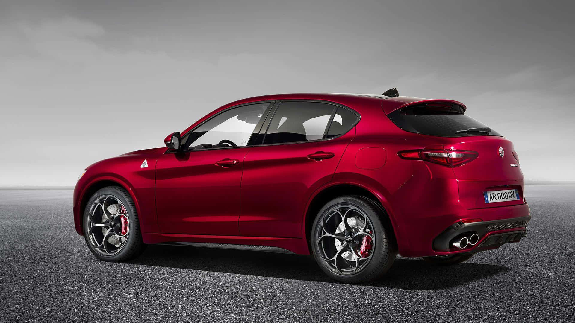 Alfa Romeo Stelvio 桌布 壁紙 — 一輛亮紅色的Alfa Romeo Stelvio SUV在灰濛濛的瀝青路面上，天空多雲。