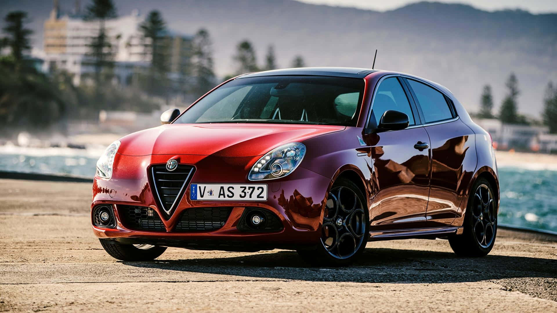 Alfa Romeo Giulia 桌布 壁紙 — 一輛亮紅色的Alfa Romeo Giulietta停泊在沿海公路，背景是海洋和山丘。