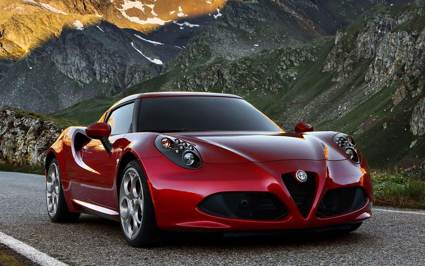 Alfa Romeo 4c 桌布 壁紙 — 一輛亮紅色的Alfa Romeo跑車停泊在一條山路上，周圍是被金色夕陽照耀的積雪山峰。