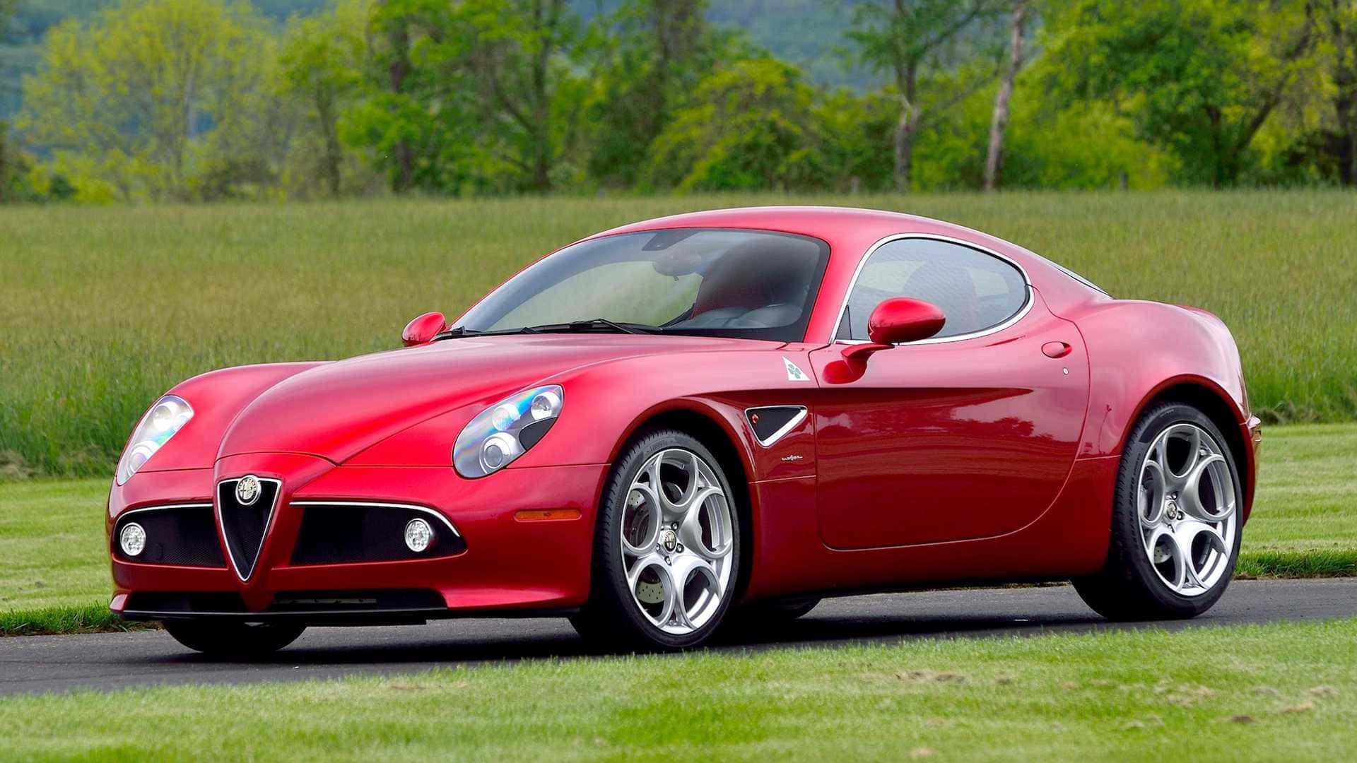 Alfa Romeo 8c Competizione 桌布 壁紙 — 一輛亮紅色的Alfa Romeo跑車停放在鋪砌的道路上，旁邊是一片草地，背景有綠色樹木。