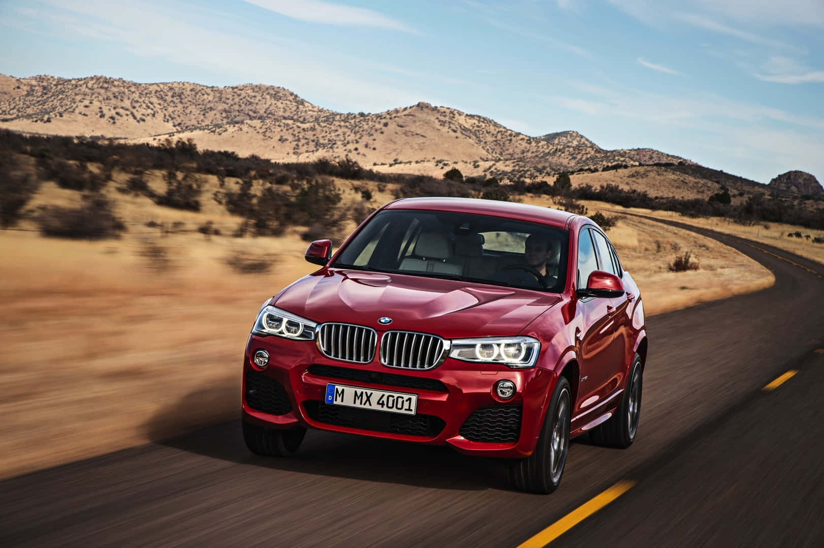 Bmw X4 桌布 壁紙 — 一輛亮紅色的BMW X4在乾燥丘陵和晴朗藍天下沿著蜿蜒的沙漠道路巡航。