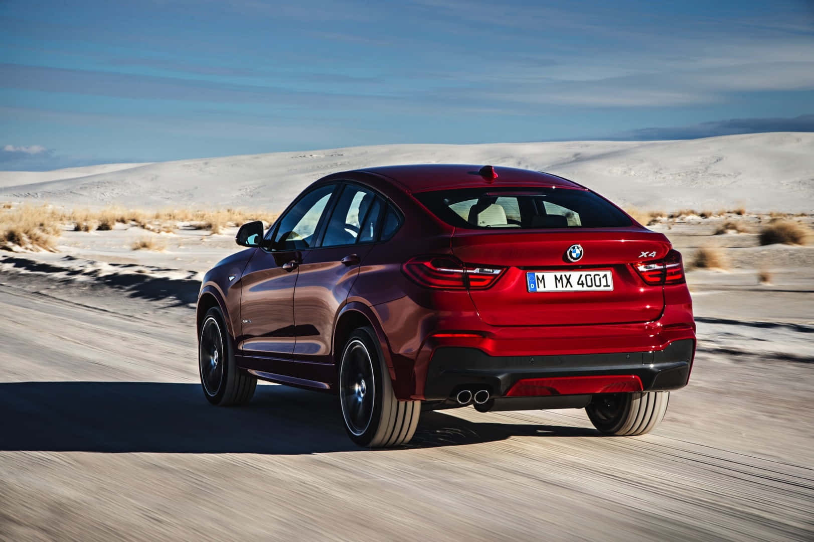 Bmw X4 桌布 壁紙 — 一輛亮紅色的BMW X4在白色沙丘和乾草叢生的沙漠道路上行駛，天空湛藍清澈。