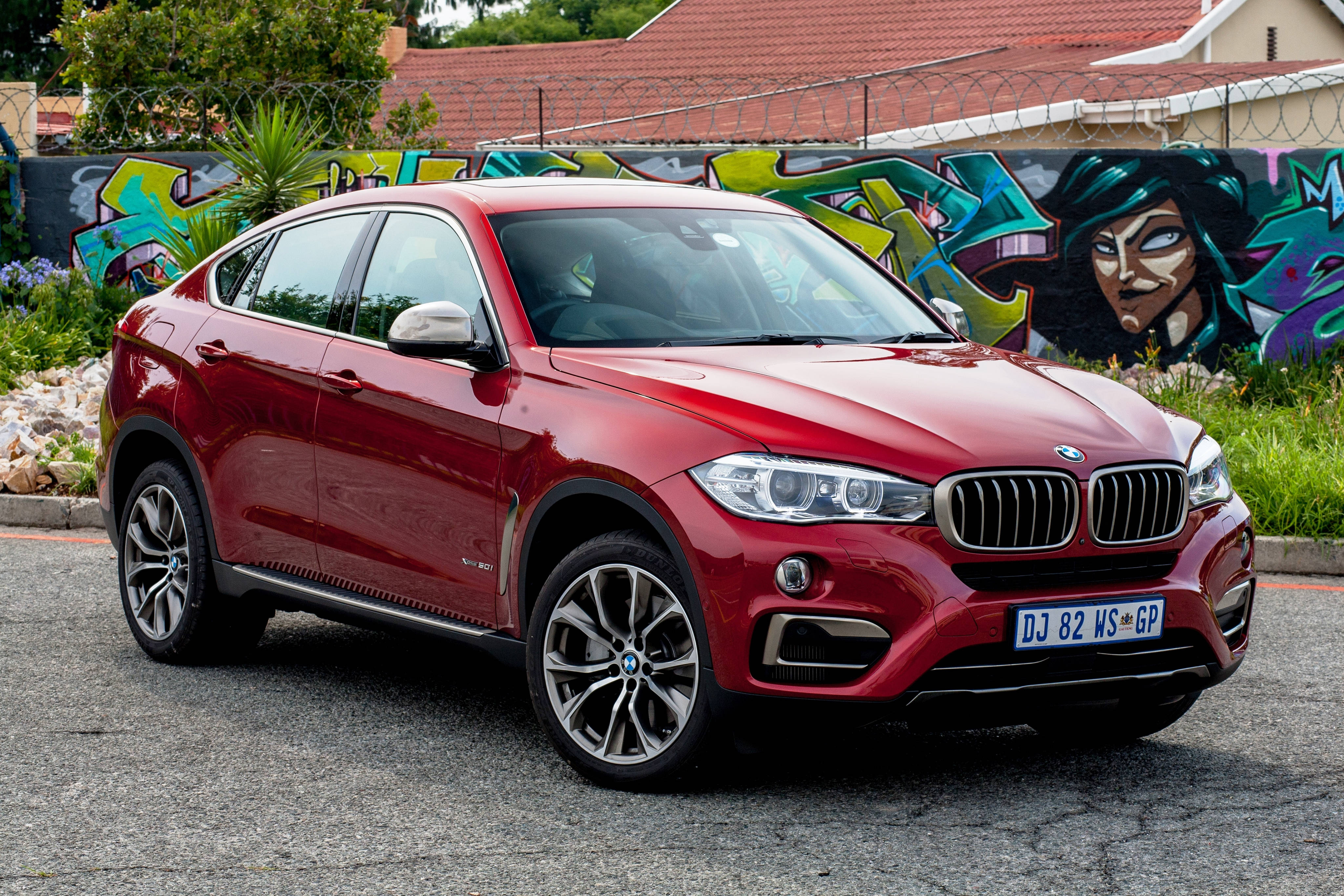 Bmw X6 M 桌布 壁紙 — 一輛亮紅色的BMW X6 SUV停在瀝青路上，背後是充滿活力的塗鴉牆。