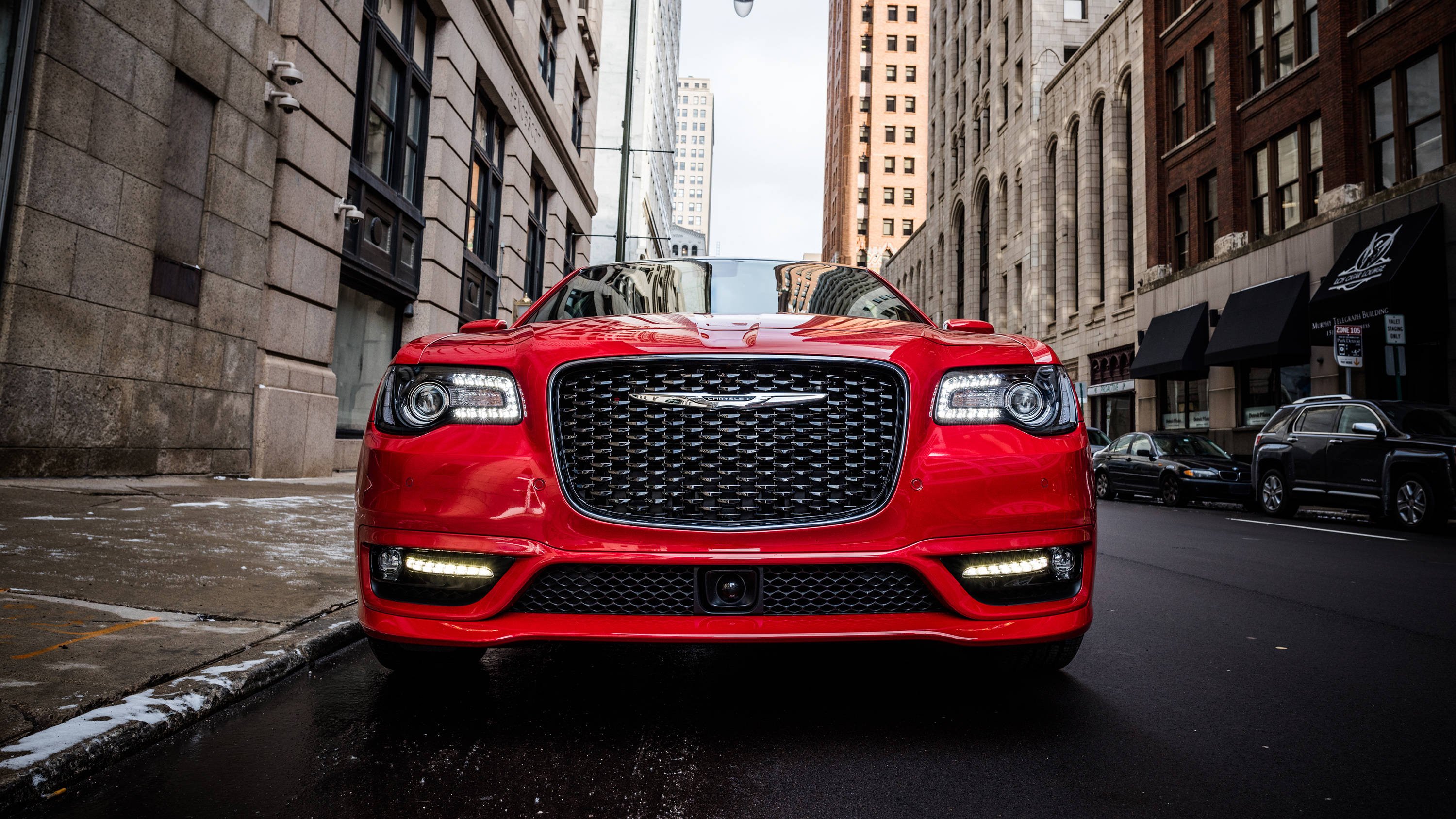 Chrysler 桌布 壁紙 — 一輛亮紅色的Chrysler 300C敞篷車停放在濕滑的城市街道上，兩旁是高聳的磚造建築，天空多雲。