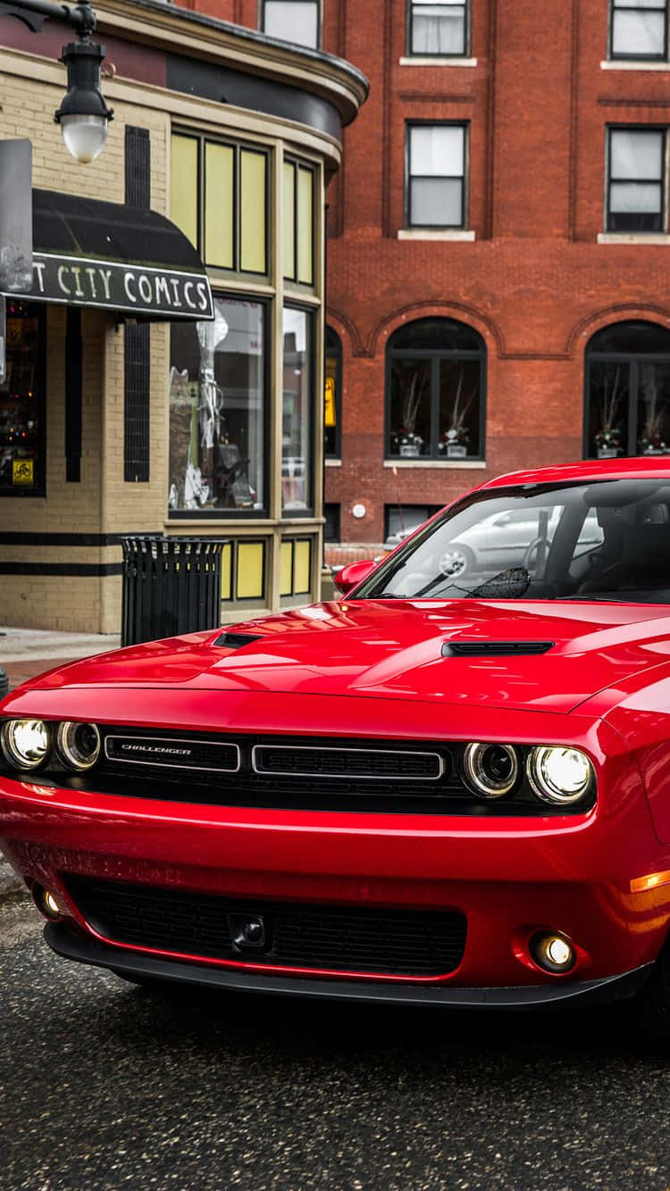 桌布 壁紙 — 一輛亮紅色的Dodge Challenger停在城市街道上，旁邊是一棟有漫畫店遮陽篷的磚建築。