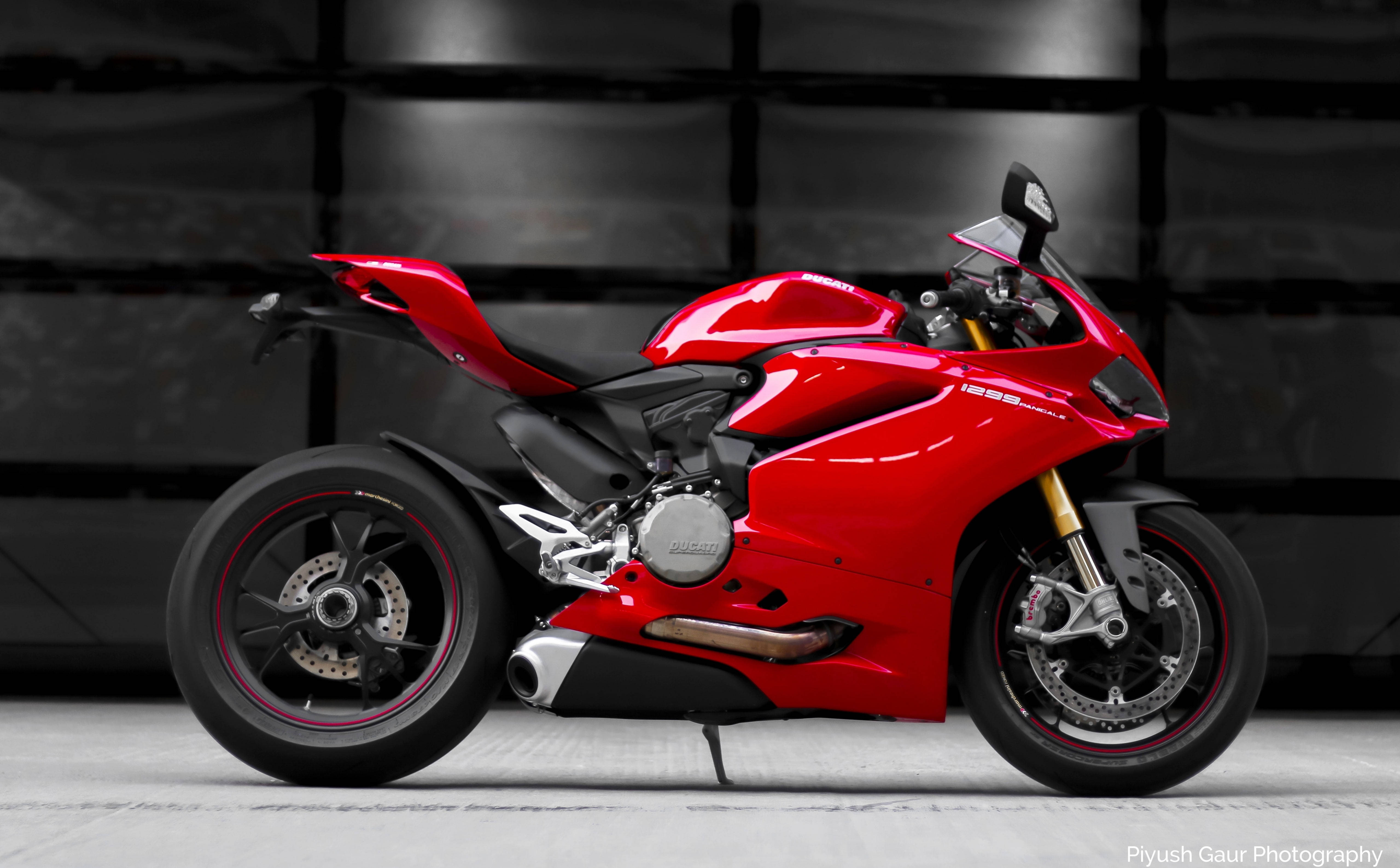 機車 桌布 壁紙 — 一輛亮紅色的Ducati摩托車在時尚的攝影棚中，黑色瓷磚牆壁和灰色地板襯托下，蓄勢待發。