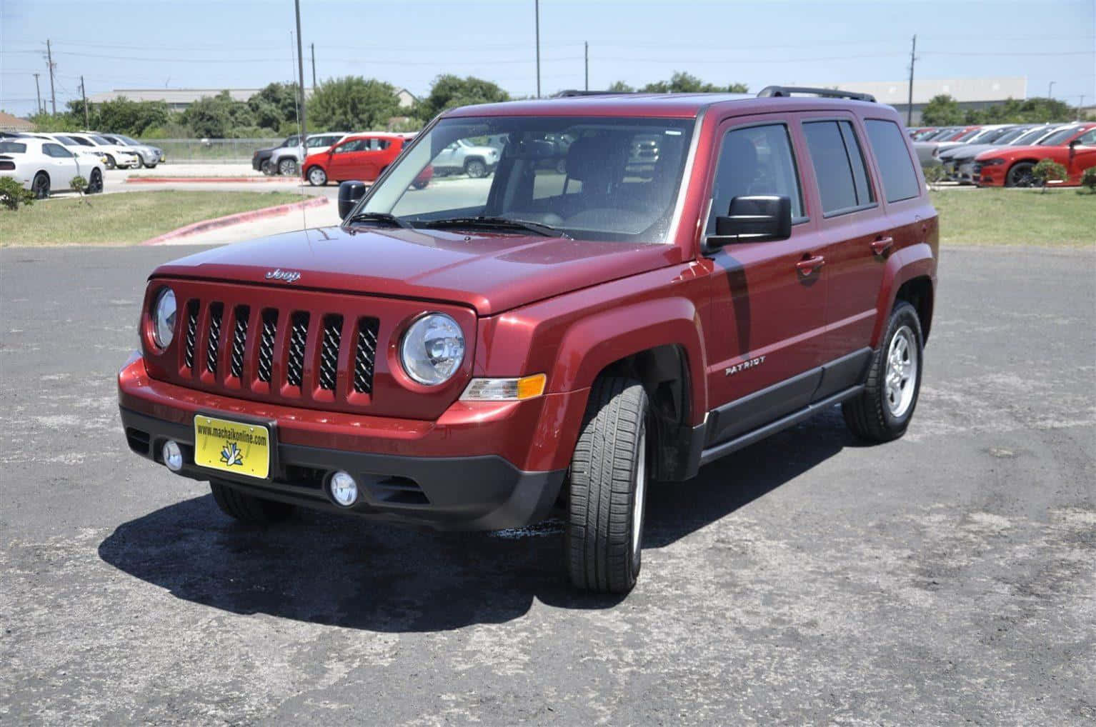 Jeep Patriot 桌布 壁紙 — 一輛亮紅色的Jeep Patriot SUV停放在陽光明媚的瀝青停車場，背景有其他汽車和綠樹。