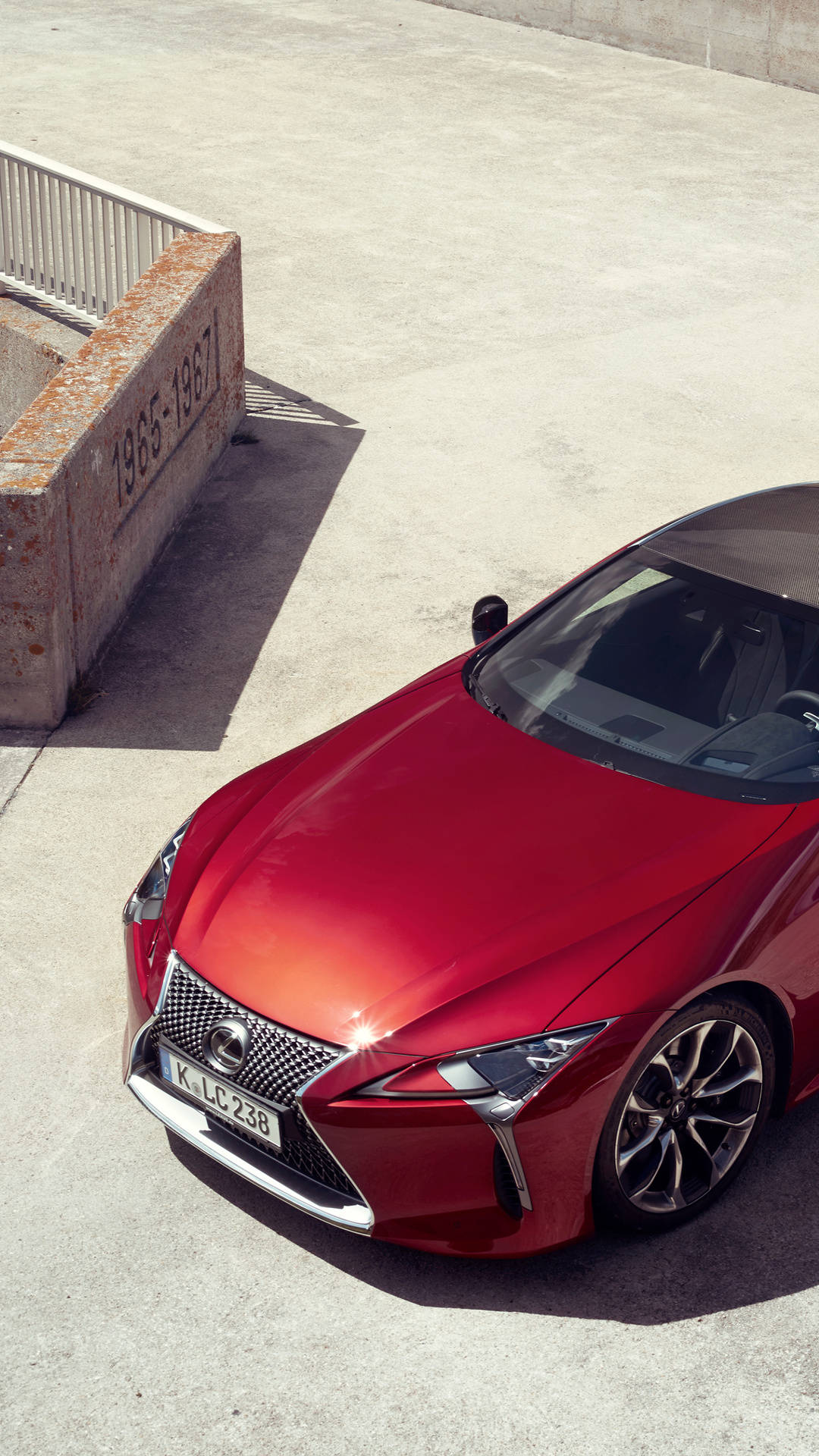 lexus iPhone 桌布 壁紙 — 一輛亮紅色的Lexus LC 230跑車停在混凝土上，在明亮的日光下投射出清晰的陰影。