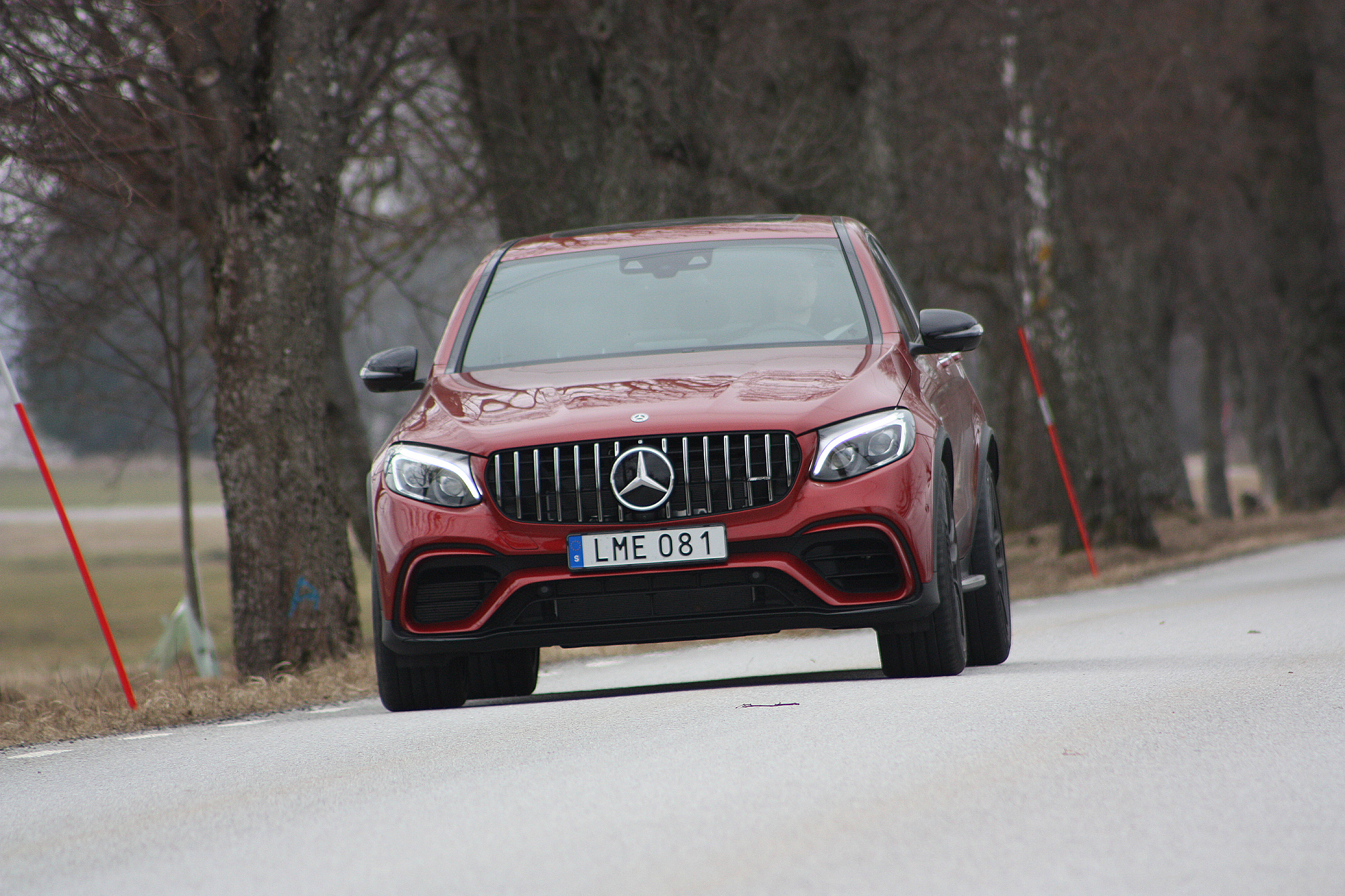 Mercedes Amg 桌布 壁紙 — 一輛亮紅色的Mercedes-AMG GLE63 S SUV在陰天自信地行駛在綠樹成蔭的道路上。
