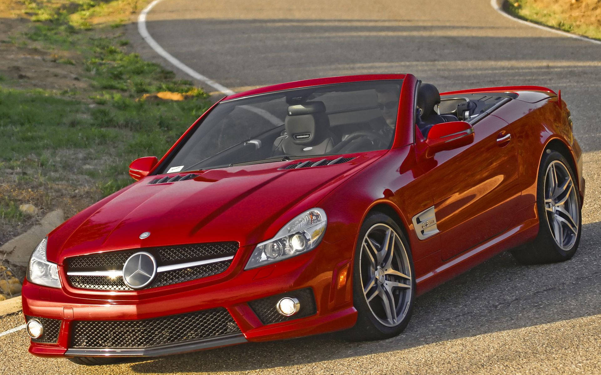 Mercedes 桌布 壁紙 — 一輛亮紅色的Mercedes-Benz SLR McLaren敞篷跑車停泊在陽光明媚、彎曲的瀝青路上，路肩有草。