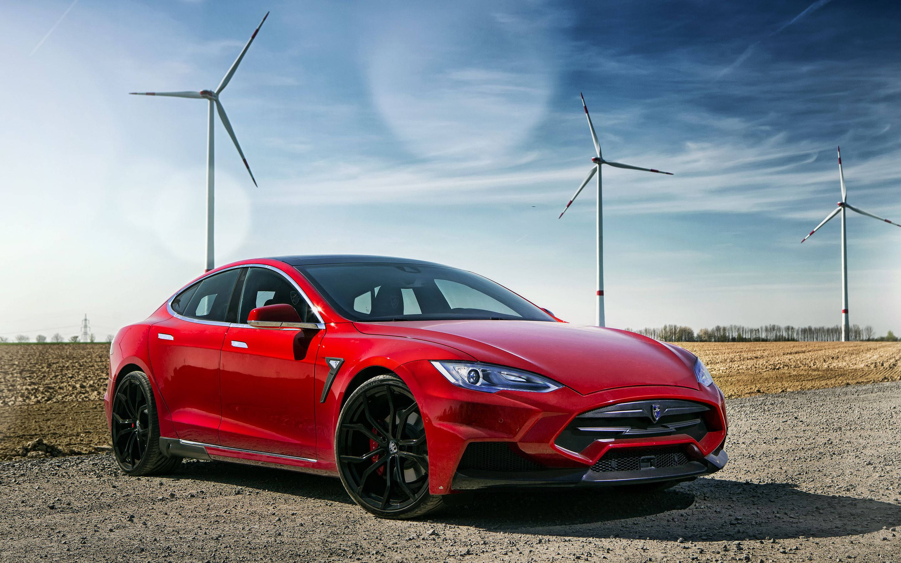 特斯拉 桌布 壁紙 — 一輛亮紅色的Tesla Model S Performance停泊在碎石上，三座風力發電機高聳在明亮的藍天下。