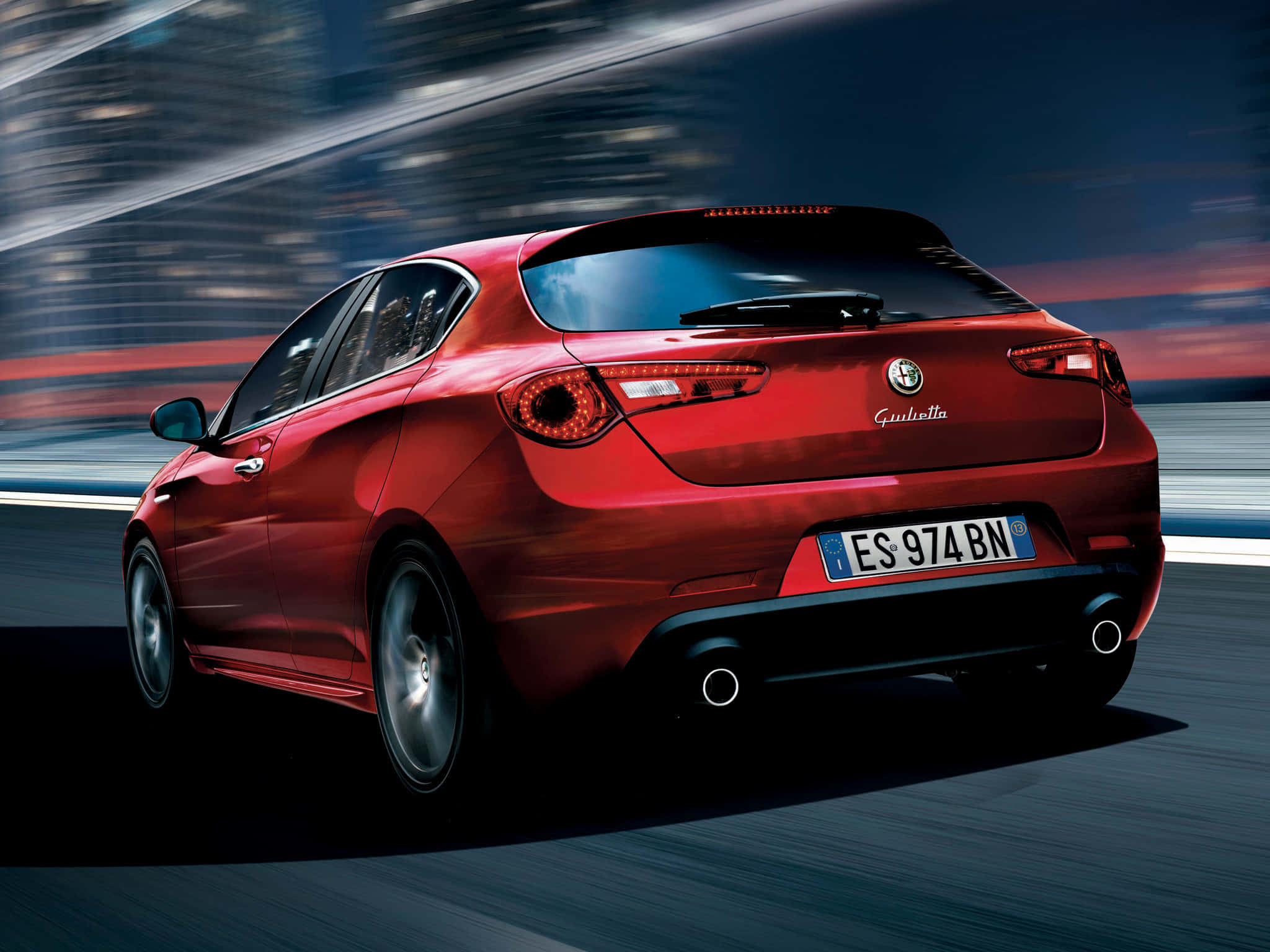 Alfa Romeo Giulietta 桌布 壁紙 — 一輛亮紅色的愛快羅密歐Giulietta在黃昏時分沿著模糊的高速公路疾駛，背景是流動的城市燈光。