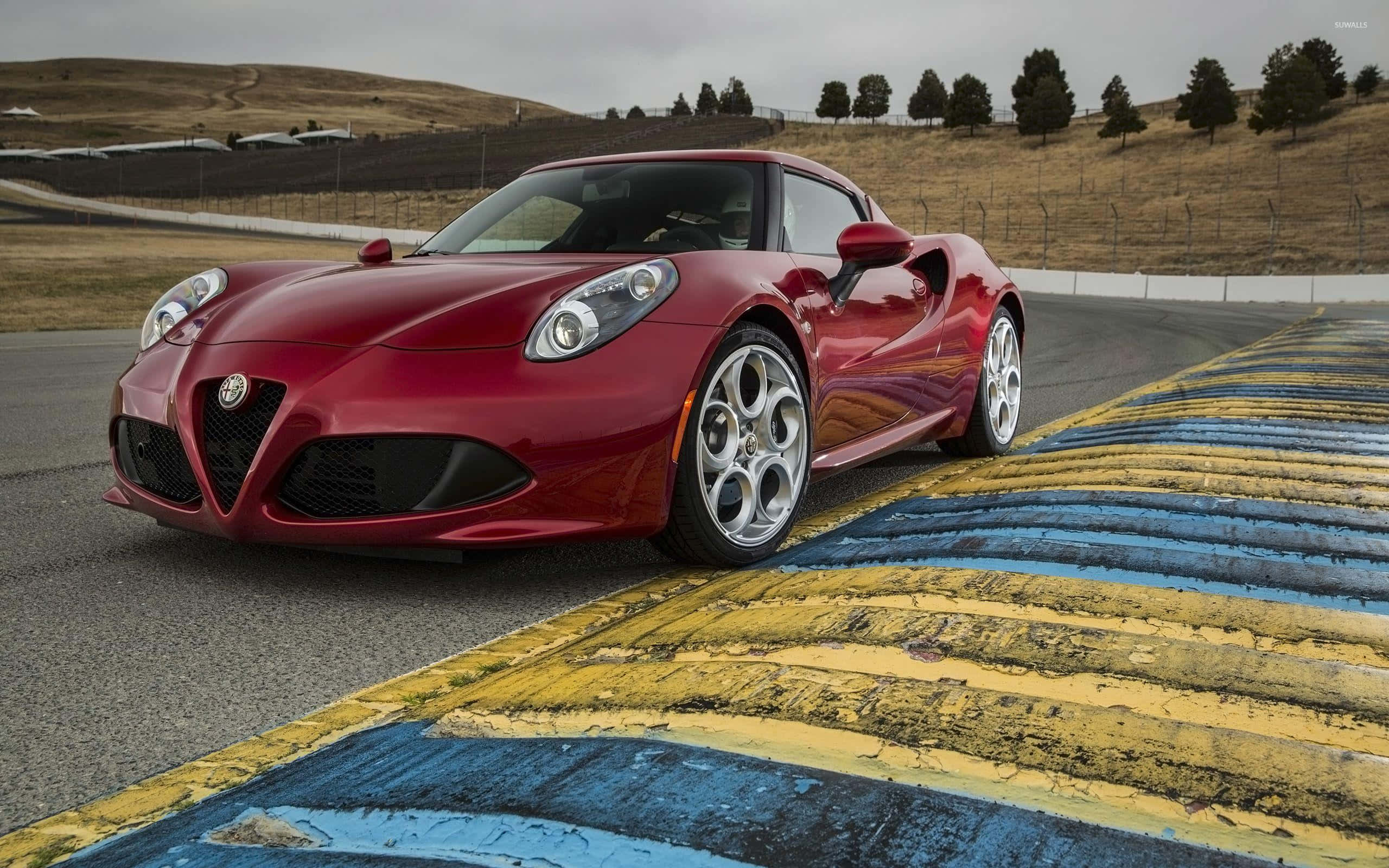 Alfa Romeo 4c 桌布 壁紙 — 一輛亮紅色的愛快羅密歐跑車在陰天之下，沿著一條帶有風化黃藍色路緣的賽道疾馳。