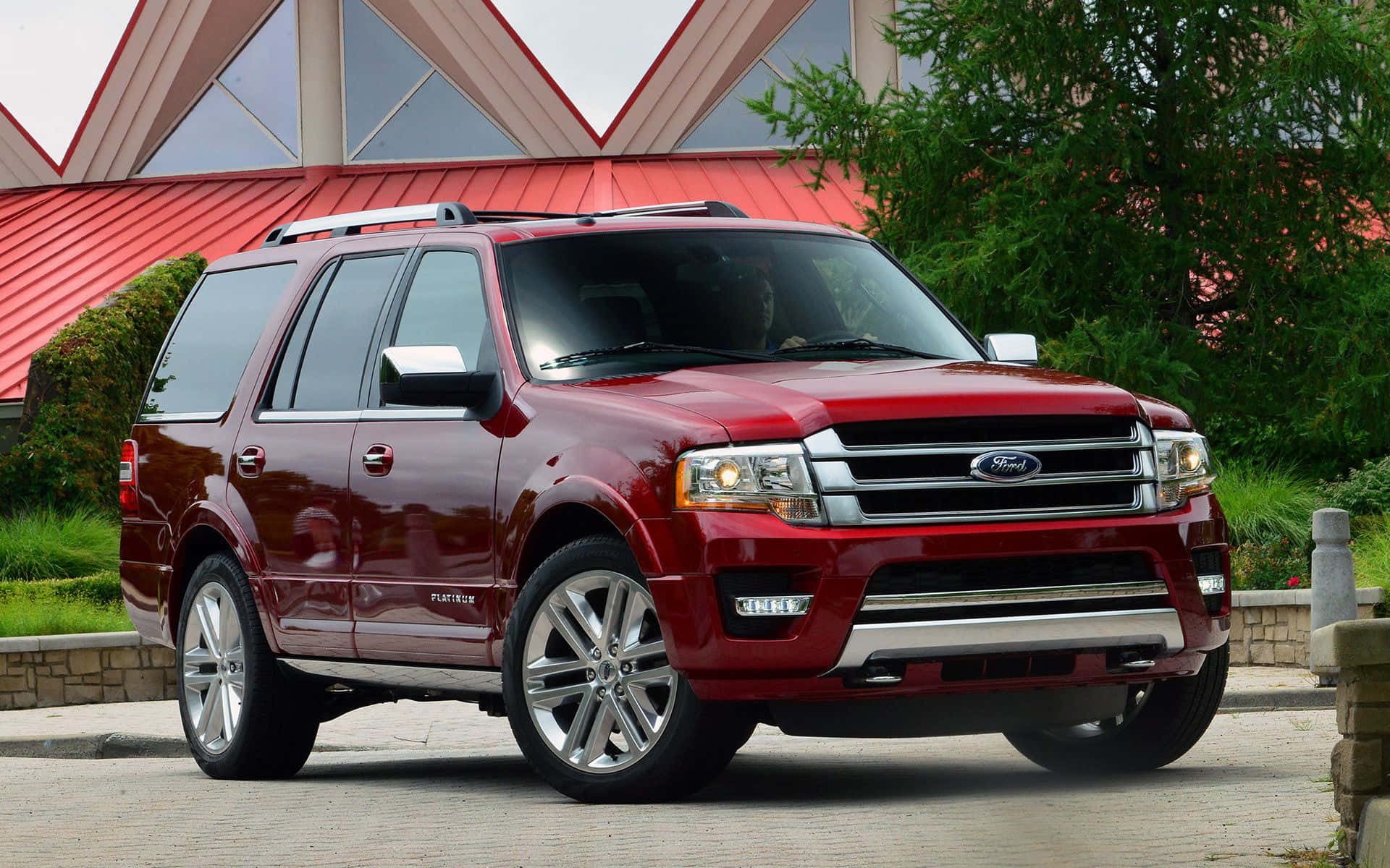 Ford Expedition 桌布 壁紙 — 一輛亮紅色的福特 Expedition SUV 停放在石頭車道上，背景有現代建築和綠植。