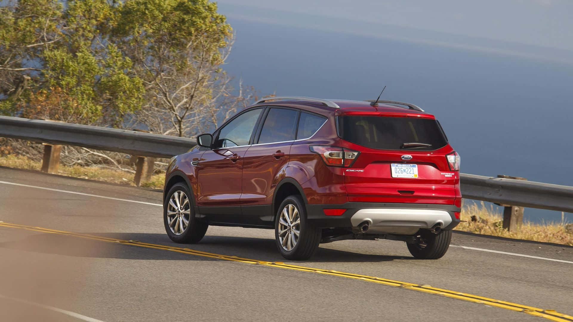 Ford Escape 桌布 壁紙 — 一輛亮紅色的福特Escape SUV沿著海岸公路行駛，背景是海洋和樹木。