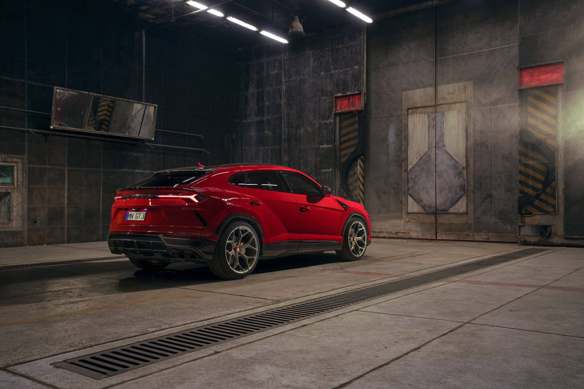 lambo 桌布 壁紙 — 一輛亮紅色的藍寶堅尼 Urus SUV 停放在骯髒的工業車庫中，在刺眼的螢光燈下。