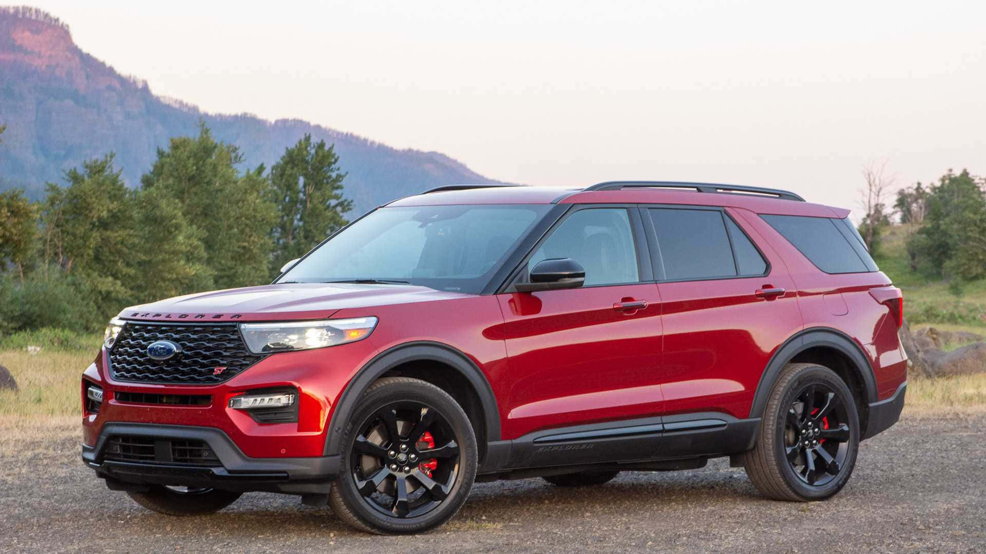 Ford Explorer 桌布 壁紙 — 一輛亮紅色福特Explorer SUV，帶黑色飾邊，停在碎石地上，背景是黃昏時分的森林山脈。