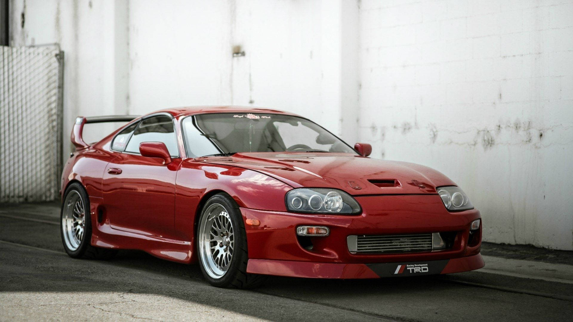 紅色豐田Supra跑車停泊在帶有塗鴉的白色磚牆前。 — Toyota Supra Mk4 壁紙