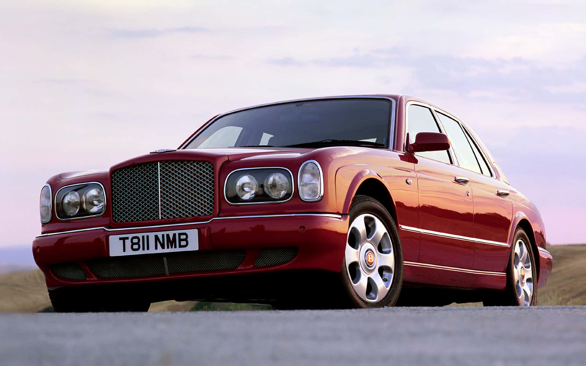 Bentley Arnage 桌布 壁紙 — 一輛亮紅色賓利 Continental 豪華轎車停放在鋪砌道路上，背景是柔和的暮色天空。