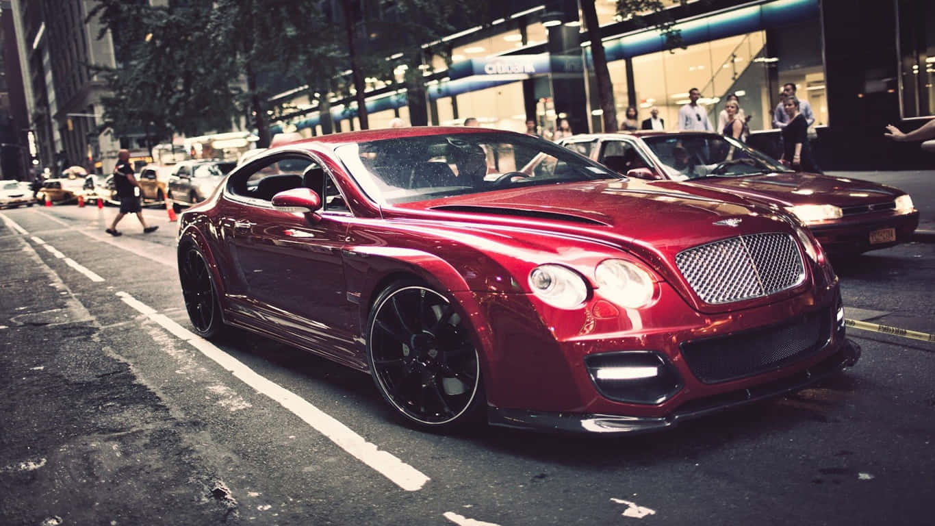 1366x768 Bentley 桌布 壁紙 — 一輛亮紅色賓利 Continental GT 跑車停泊在濕漉漉的城市街道上，背景有行人和商店門面。