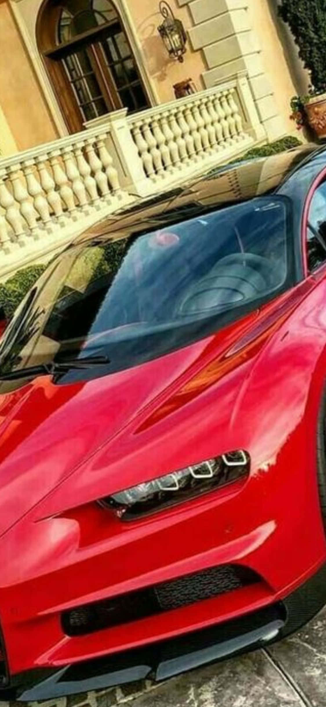 iPhone Xs Bugatti 桌布 壁紙 — 一輛亮紅色跑車停放在豪華米色豪宅前，配有白色欄杆。