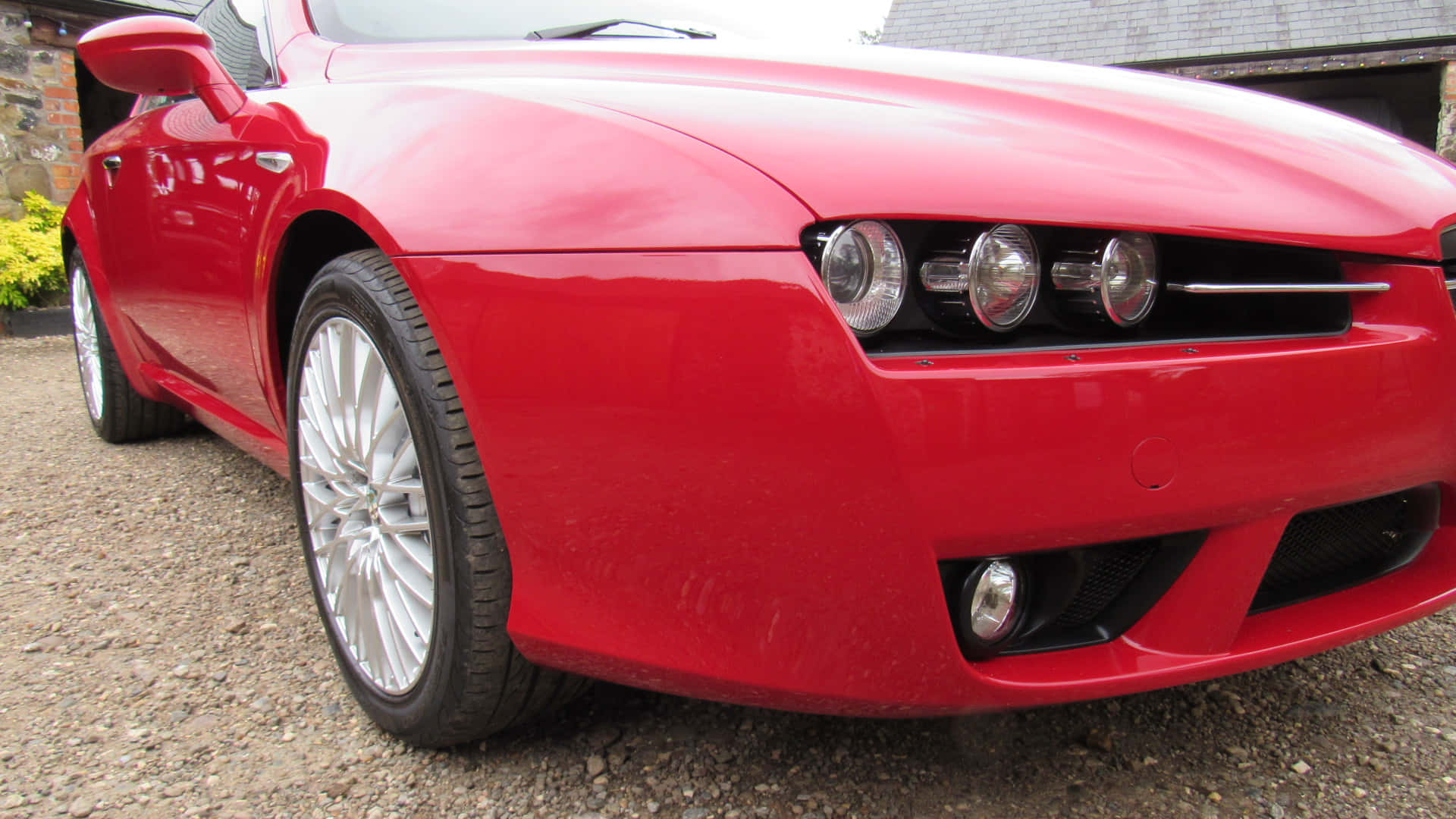 Alfa Romeo Brera 桌布 壁紙 — 一輛亮紅色跑車配銀色輪圈，停放在石建築附近的碎石地上。