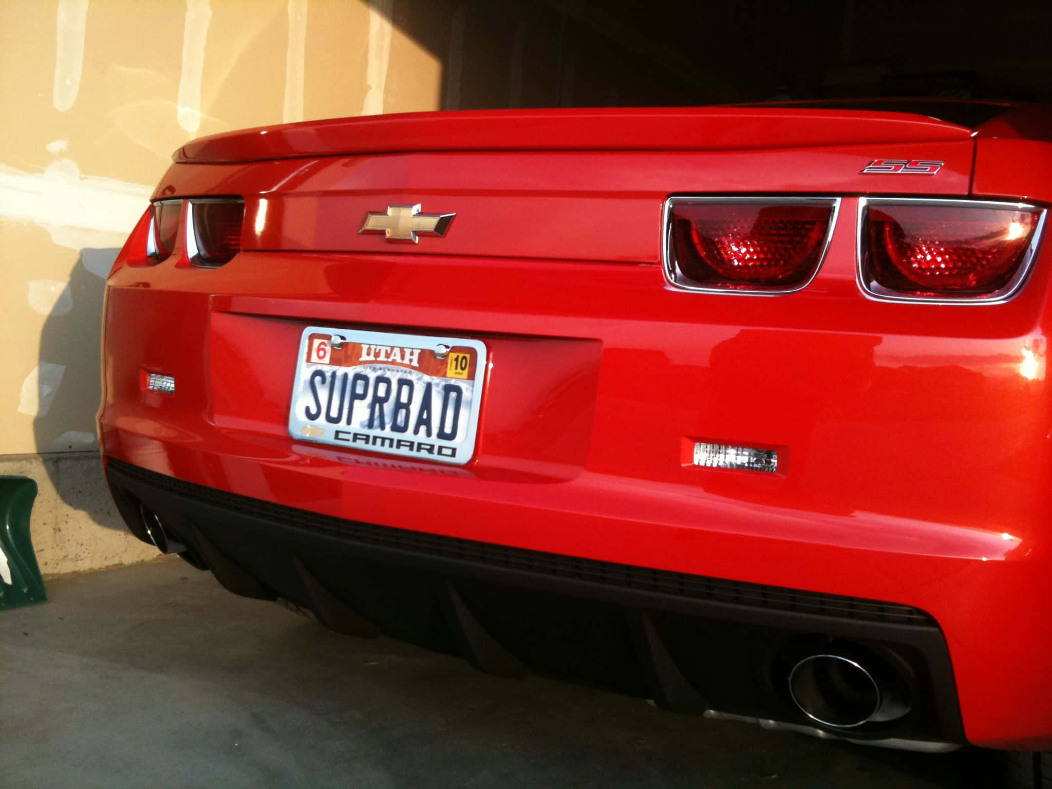 Car License Plate 桌布 壁紙 — 一輛亮紅色雪佛蘭Camaro SS停放在車庫中，帶有猶他州定製車牌「SUPRBAD」。