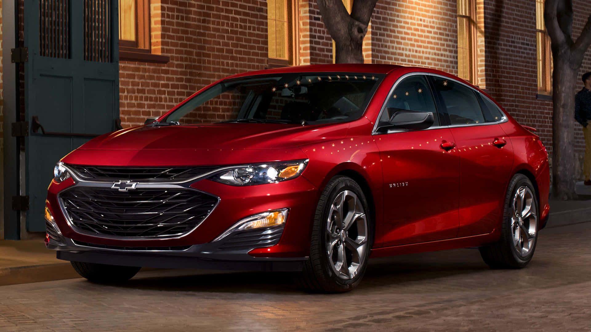 Chevy Malibu 桌布 壁紙 — 一輛亮紅色雪佛蘭轎車在夜間停泊在磚砌建築旁，建築物窗戶透出溫暖燈光。