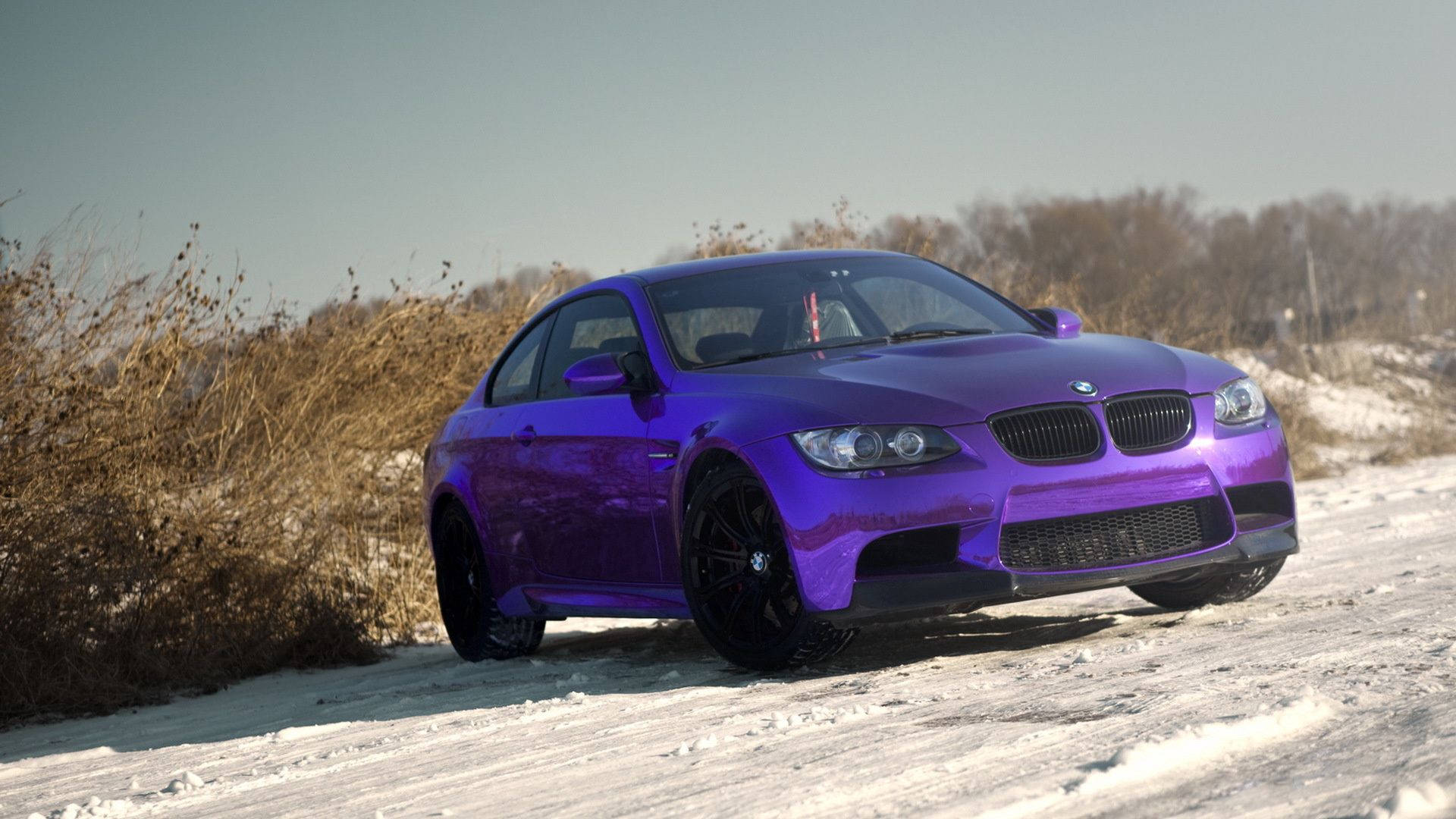Chrome 桌布 壁紙 — 一輛亮紫色BMW M3雙門跑車停在冬季積雪的路邊，周圍有乾燥的灌木和光禿禿的樹木。
