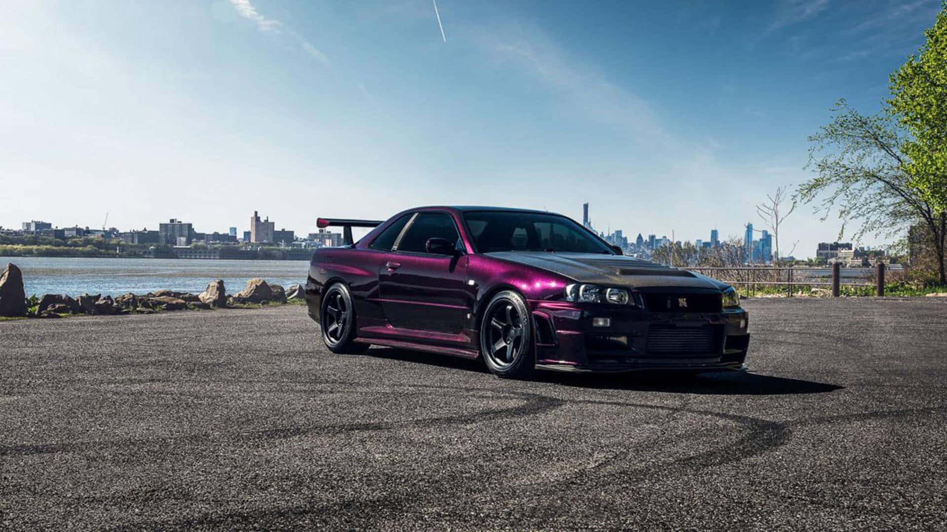 R33 GT-R 桌布 壁紙 — 一輛亮紫色跑車停在瀝青路上，背景是城市天際線和河流，天空湛藍。