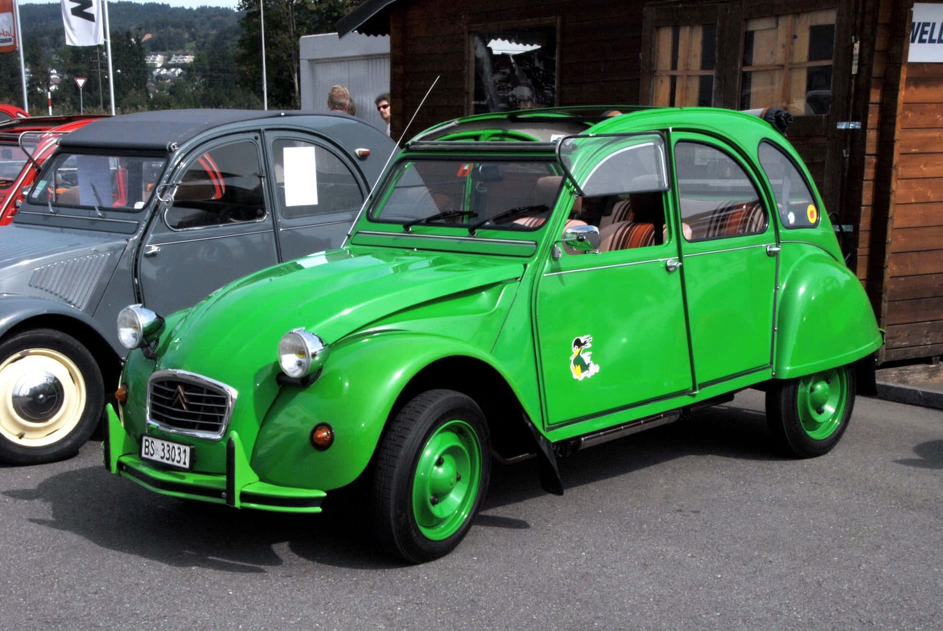 Citroen 桌布 壁紙 — 一輛亮綠色復古雪鐵龍2CV停放在戶外木建築旁，附近還有另一輛經典汽車。
