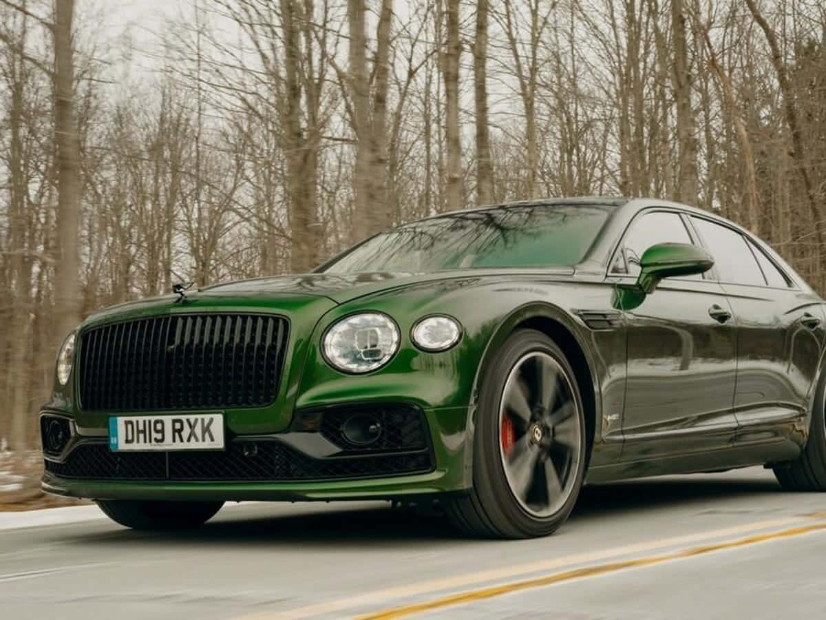Bentley Flying Spur 桌布 壁紙 — 一輛亮綠色的賓利 Flying Spur 在一條兩旁有光禿禿冬天樹木的森林道路上飛馳。