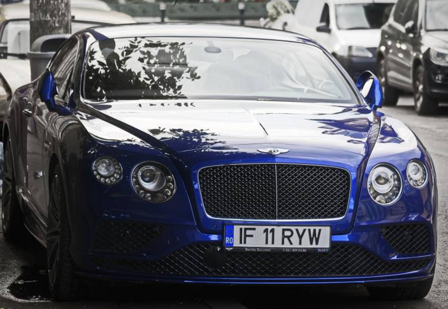 bentley HD 桌布 壁紙 — 一輛亮藍色 Bentley Continental GT 停放在濕漉漉的城市街道上，反射出樹木和周圍的汽車。