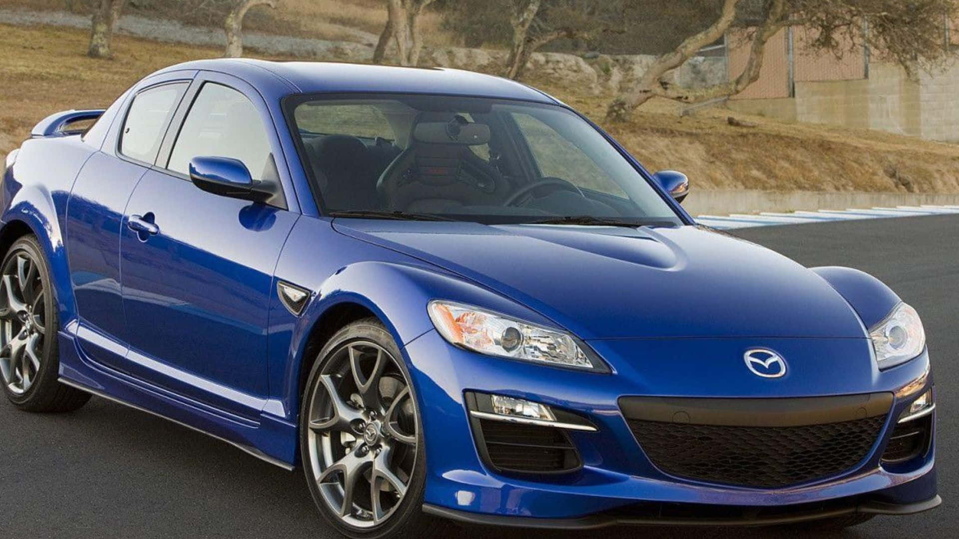 Mazda Rx-8 桌布 壁紙 — 一輛亮藍色Mazda RX-8跑車停泊在瀝青賽道上，背景有乾草和樹木。