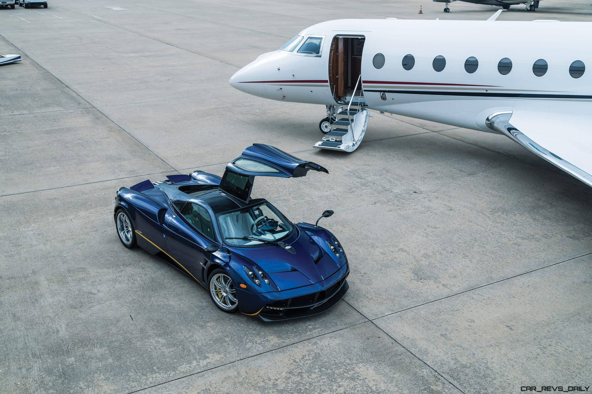 Pagani 桌布 壁紙 — 一輛亮藍色Pagani Huayra打開鷗翼車門，停在停機坪上，旁邊是一架已放下梯子的私人飛機。