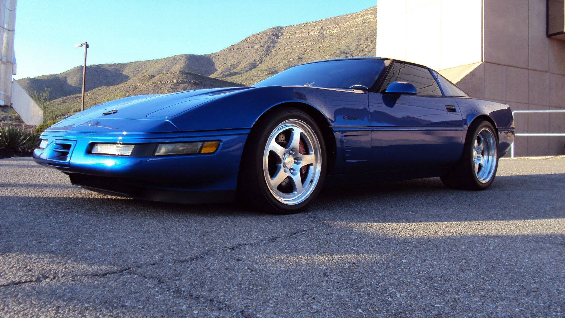 corvette 桌布 壁紙 — 一輛亮藍色跑車停在瀝青路上，背景是陽光照耀的山丘。