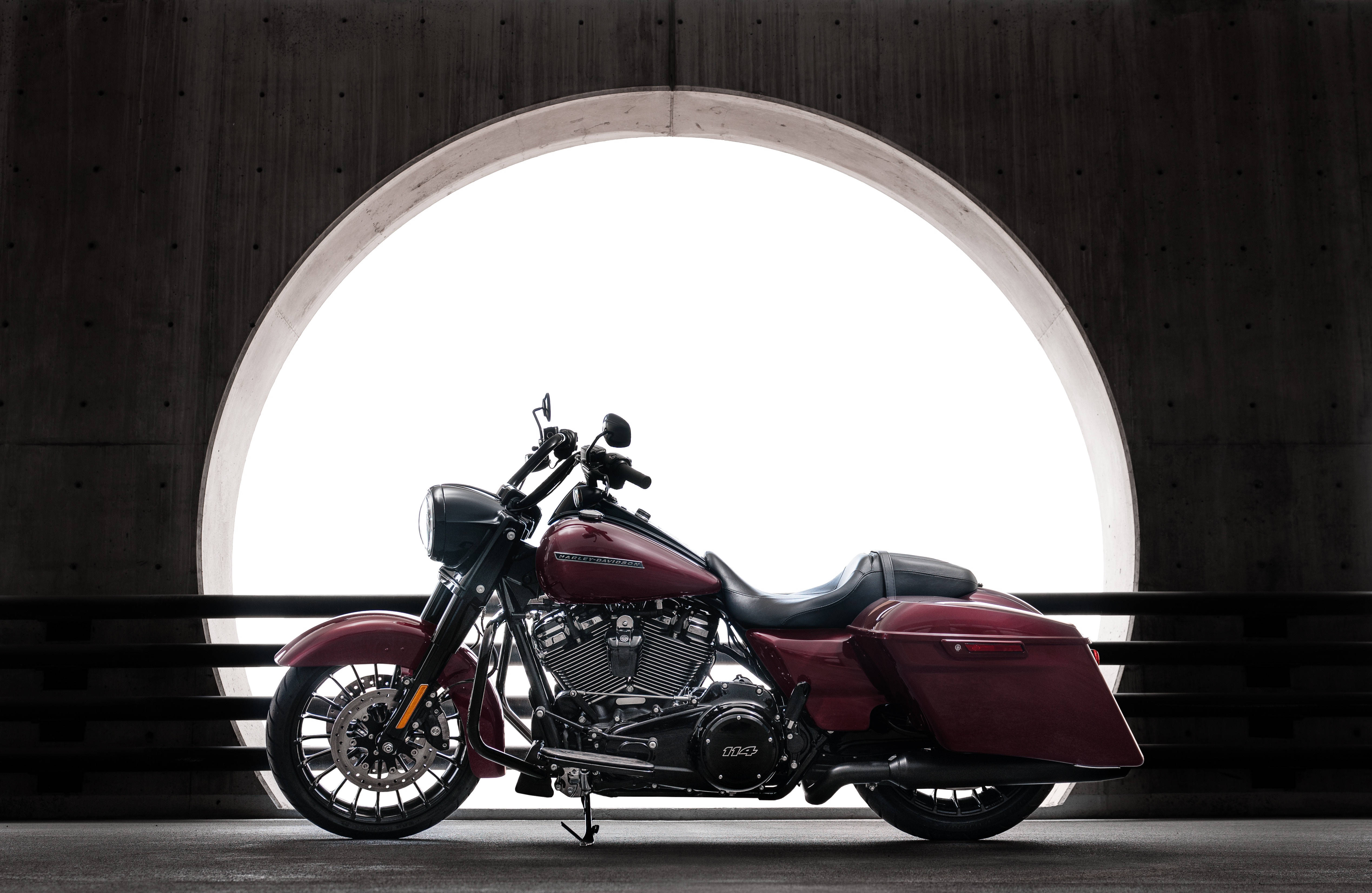 Harley 桌布 壁紙 — 一輛亮面栗色巡航機車在簡約圓形混凝土拱門下以側面姿態展示，背後有明亮背光。