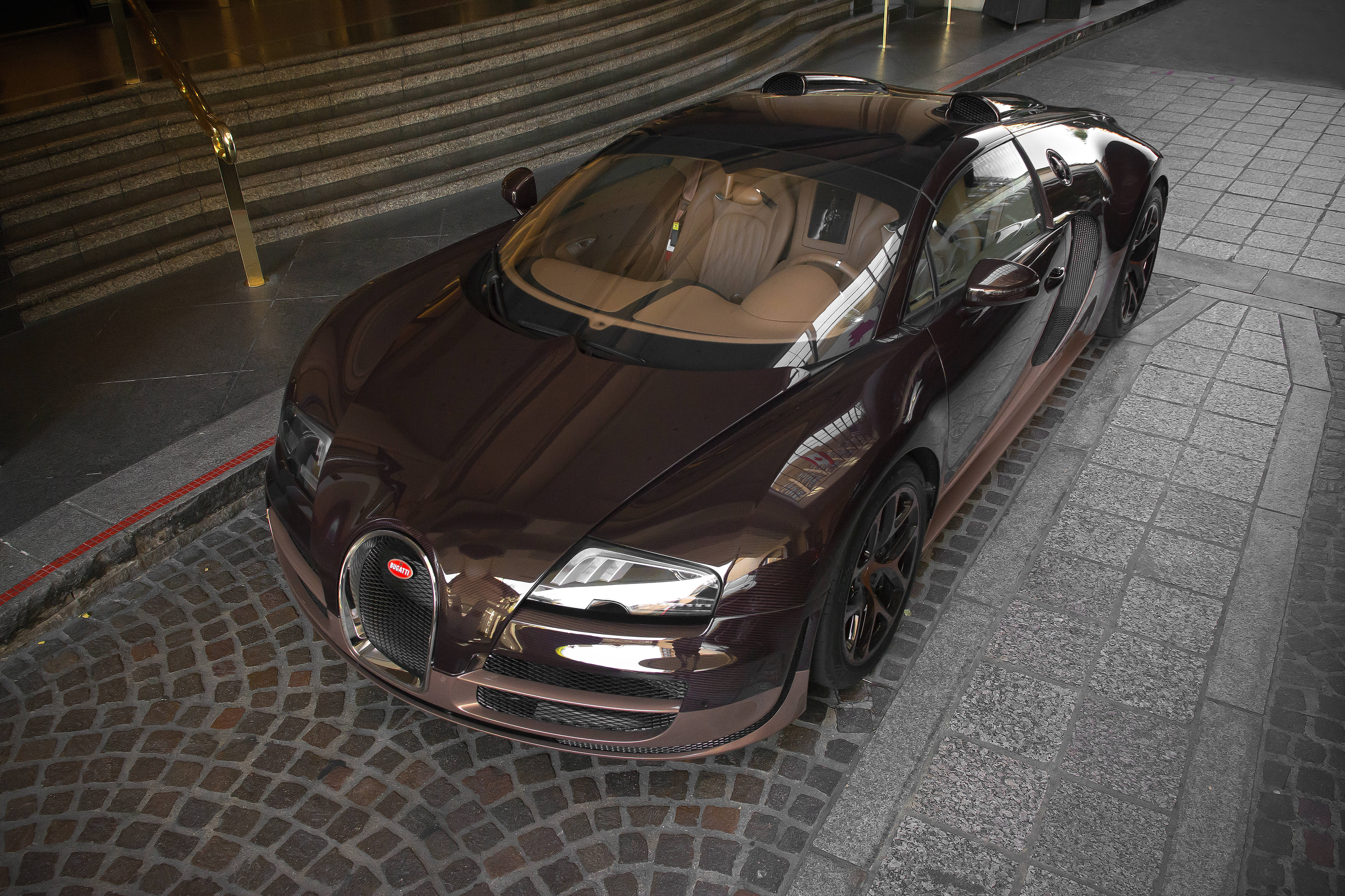 Cool Bugatti 桌布 壁紙 — 一輛亮面棕色Bugatti Veyron停泊在鵝卵石街道上，旁邊是石階，在人工燈光下。
