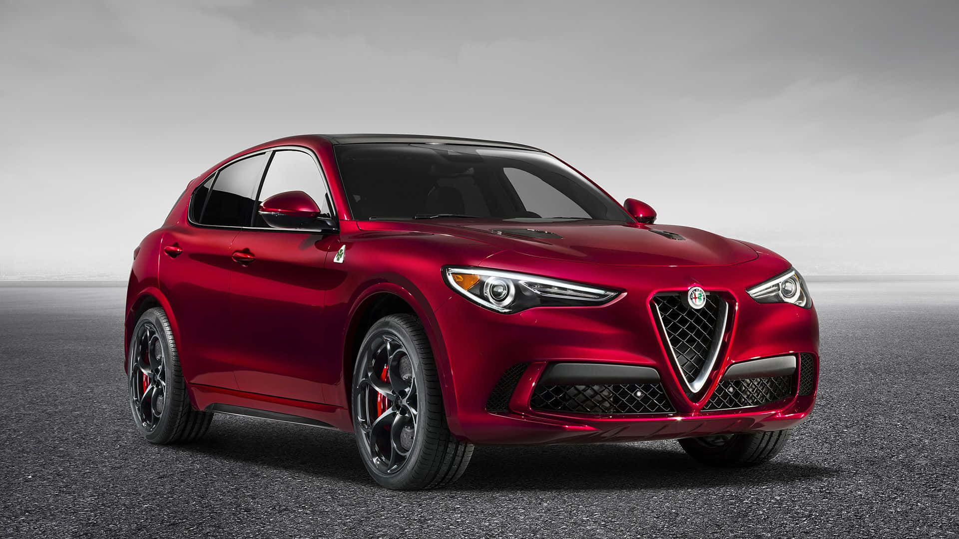 Alfa Romeo Stelvio 桌布 壁紙 — 一輛亮面紅色Alfa Romeo SUV在柔和漫射燈光下，停放在簡約灰色瀝青表面上。