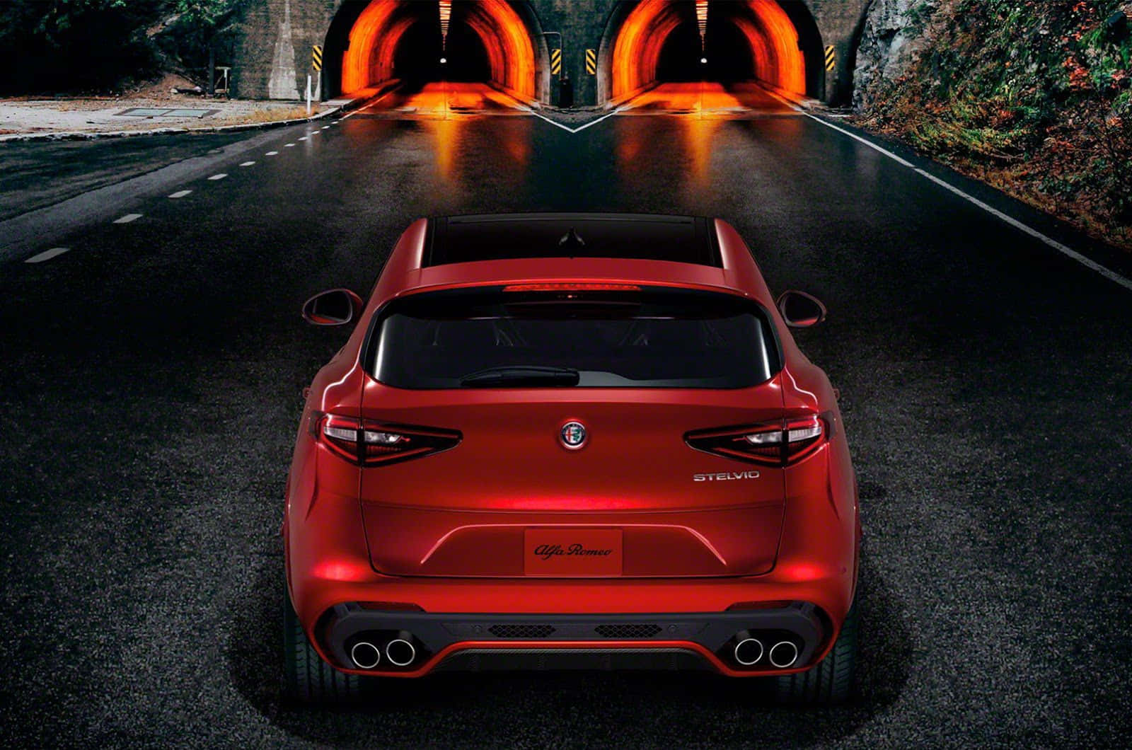 Alfa Romeo Stelvio 桌布 壁紙 — 一輛亮面紅色Alfa Romeo Stelvio SUV在夜間濕滑的瀝青路上駛向發光的橙色隧道。
