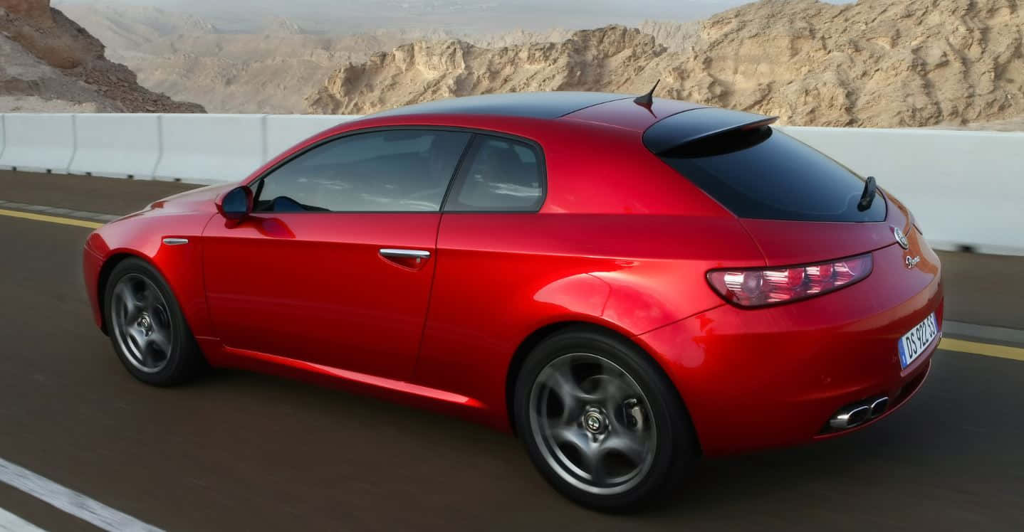 Alfa Romeo Brera 桌布 壁紙 — 一輛亮面紅色Alfa Romeo跑車在沙漠公路上行駛，背景是岩石地形。