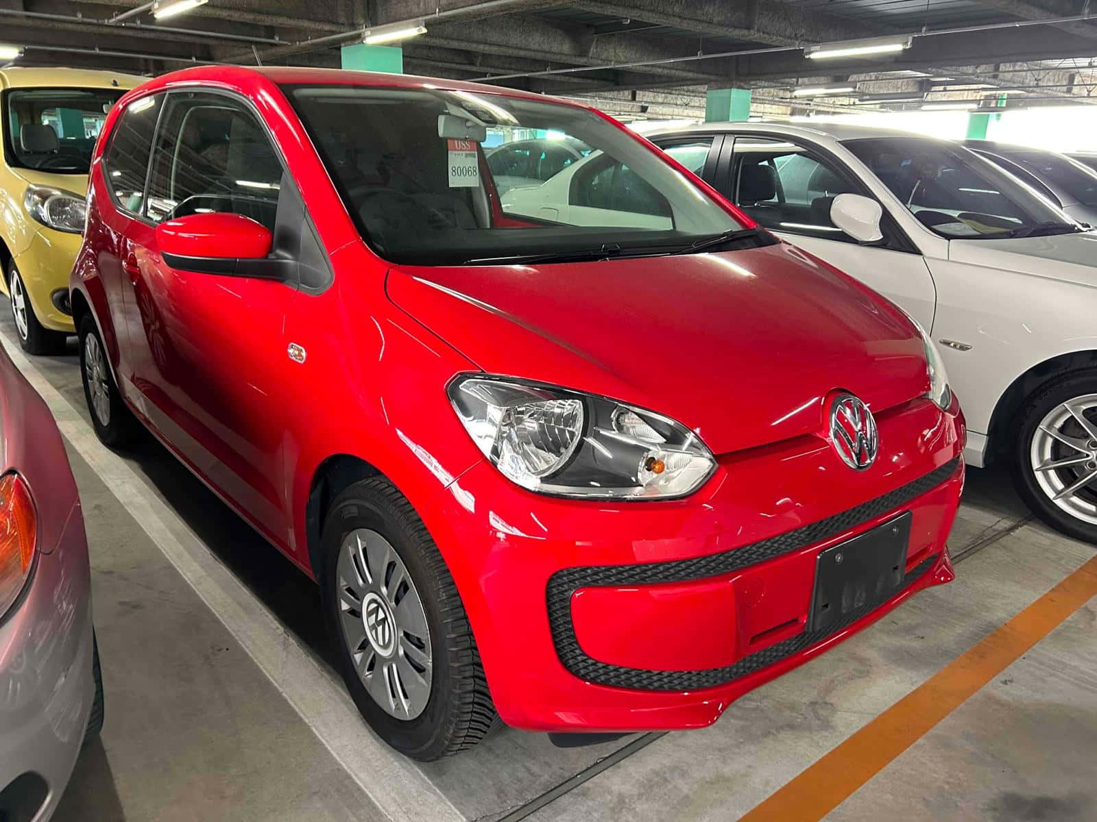  壁紙 — 一輛亮面紅色Volkswagen up!停放在光線充足的室內停車場，附近有其他車輛。
