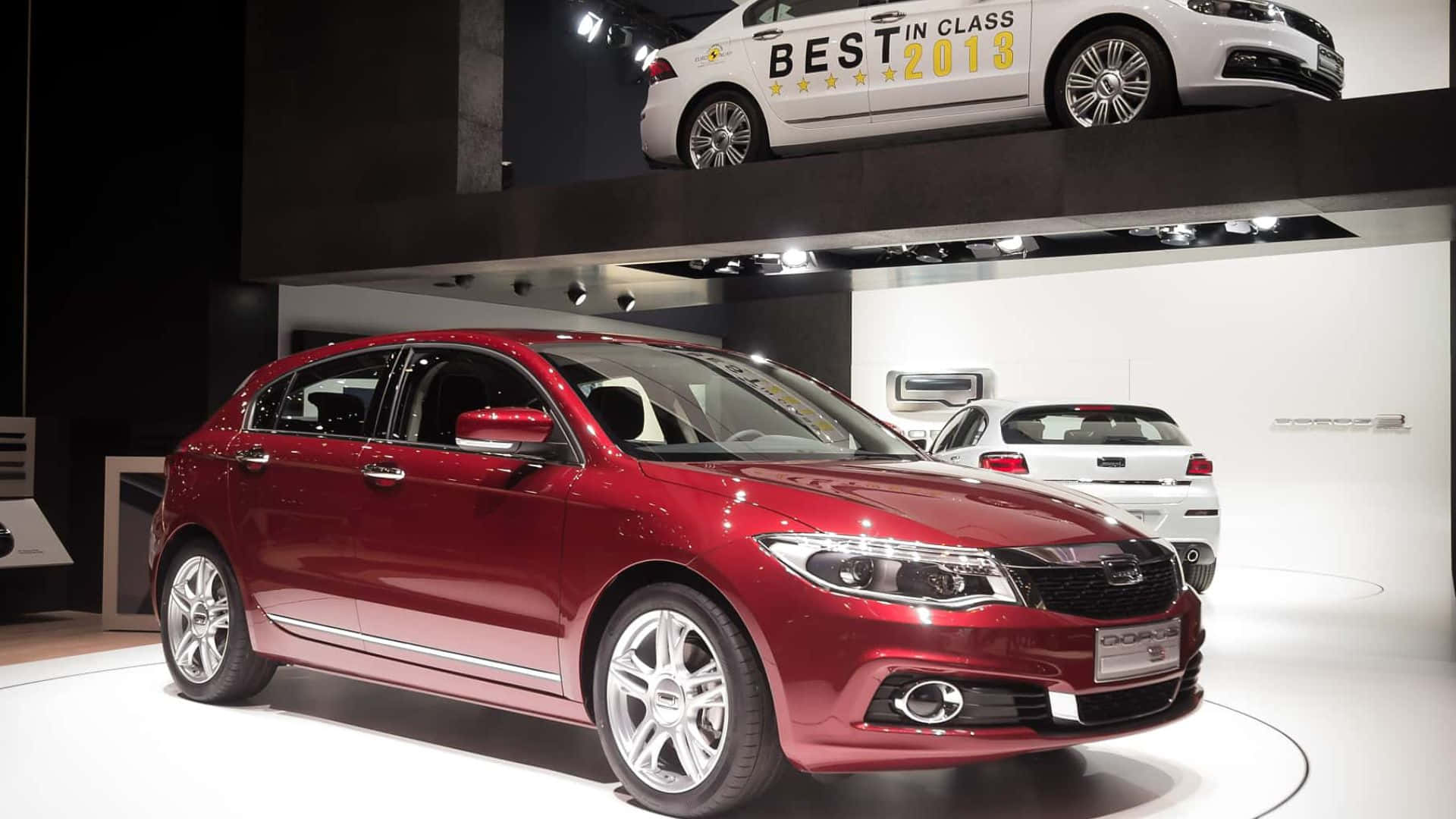 Qoros 桌布 壁紙 — 一輛亮面紅色掀背車在現代車展攤位的圓形白色平台上展示，上方有其他車輛。