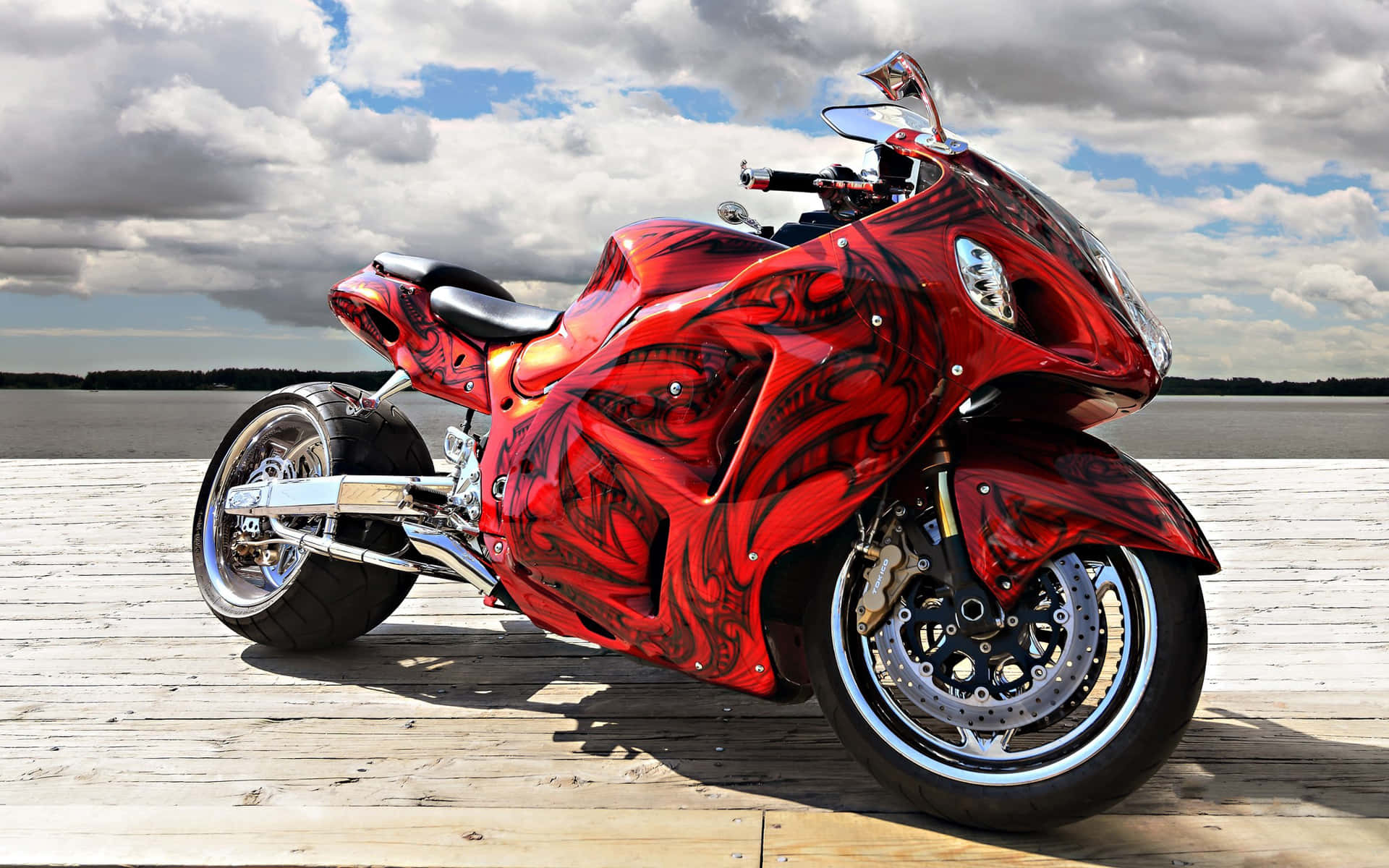 motorbike 桌布 壁紙 — 一輛亮面紅色機車帶有黑色部落圖案，停放在木製碼頭上，天空多雲。