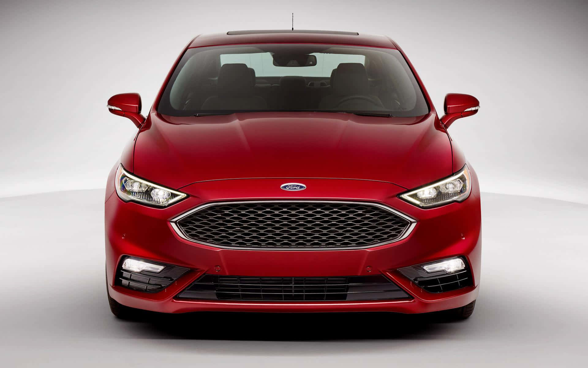 Ford Fusion 桌布 壁紙 — 一輛亮面紅色福特轎車在極簡風格的工作室中正面朝前，柔和燈光突顯其流線型現代設計。