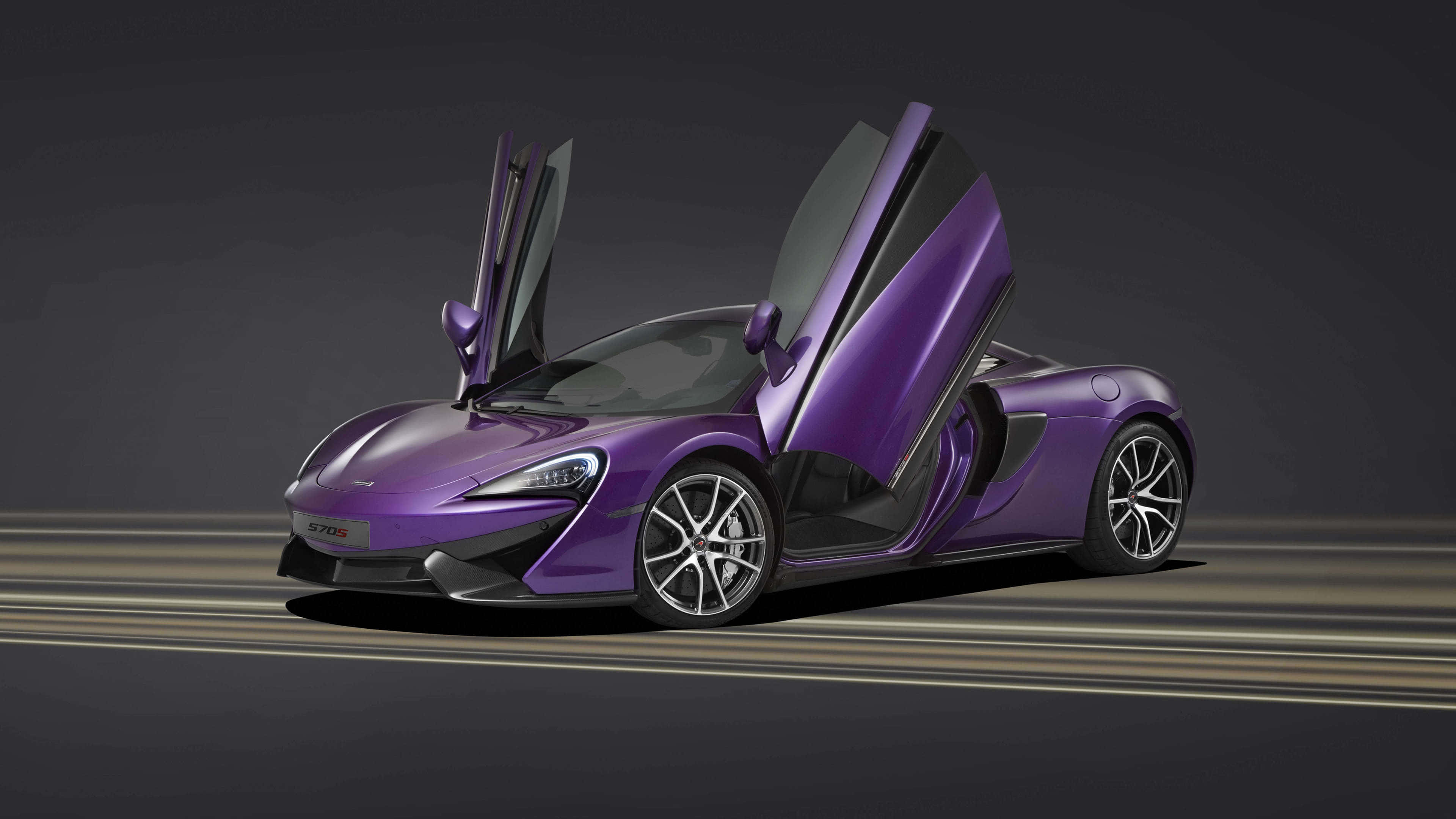 Cool Mclaren 桌布 壁紙 — 一輛亮面紫色McLaren 570S超級跑車，剪刀門打開，停在黑暗的攝影棚賽道上，帶有戲劇性燈光。