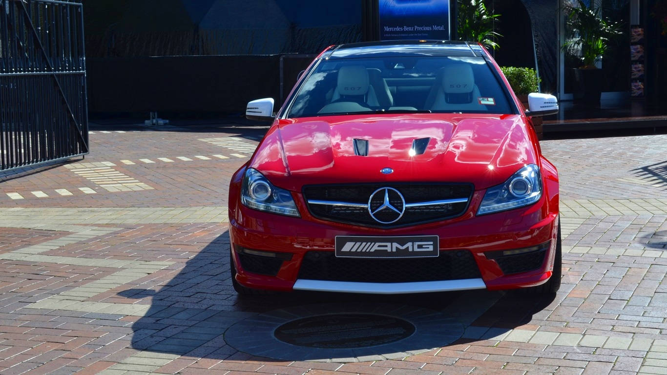 AMG iPhone 桌布 壁紙 — 一輛亮麗的紅色 Mercedes-AMG 跑車停泊在陽光普照的磚砌路面上，投射出清晰的陰影。
